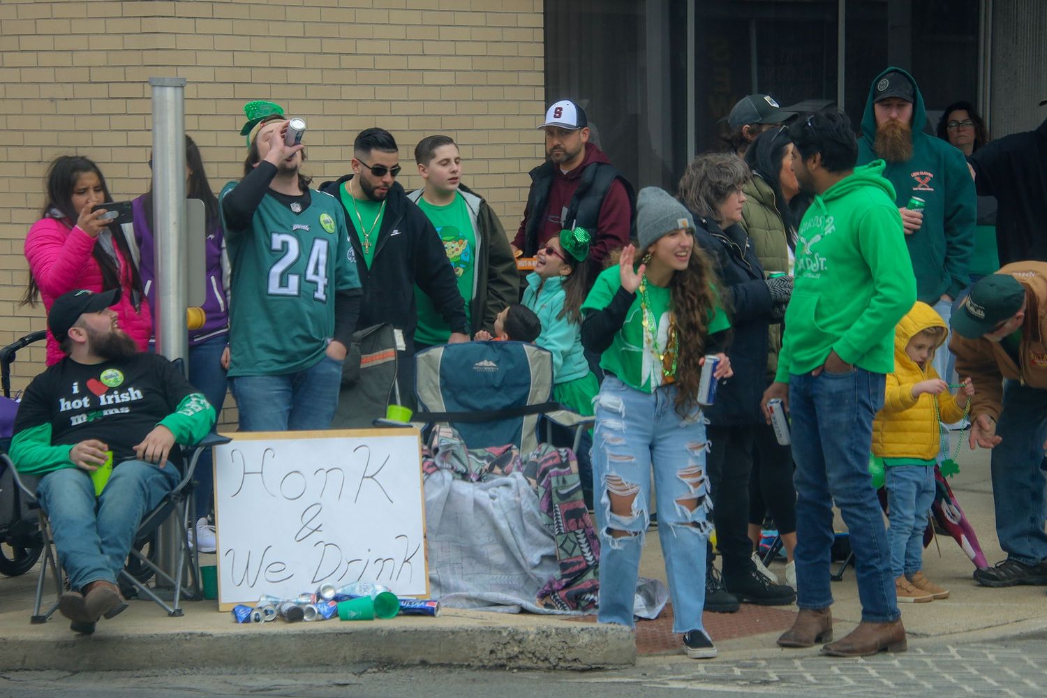 Crowd of sports fans in green jerseys gather outside stadium entrance for game day festivities.