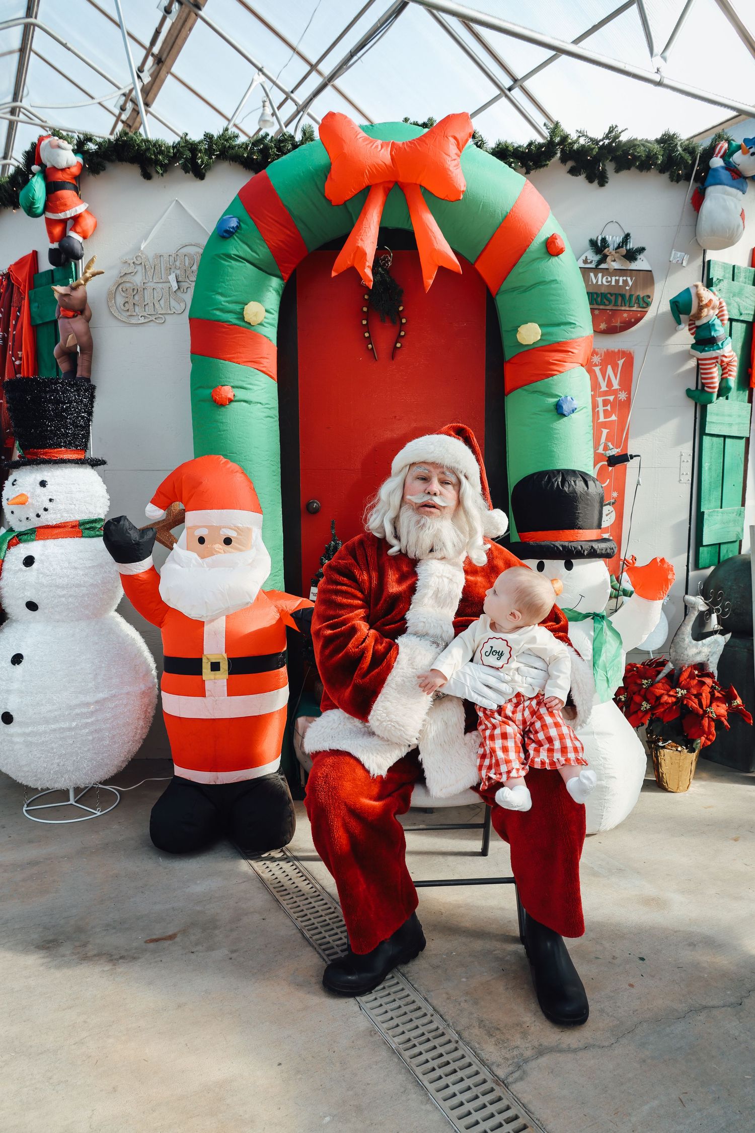 A festive holiday scene with inflatable snowmen and Santas around a large green archway decorated with a red bow.