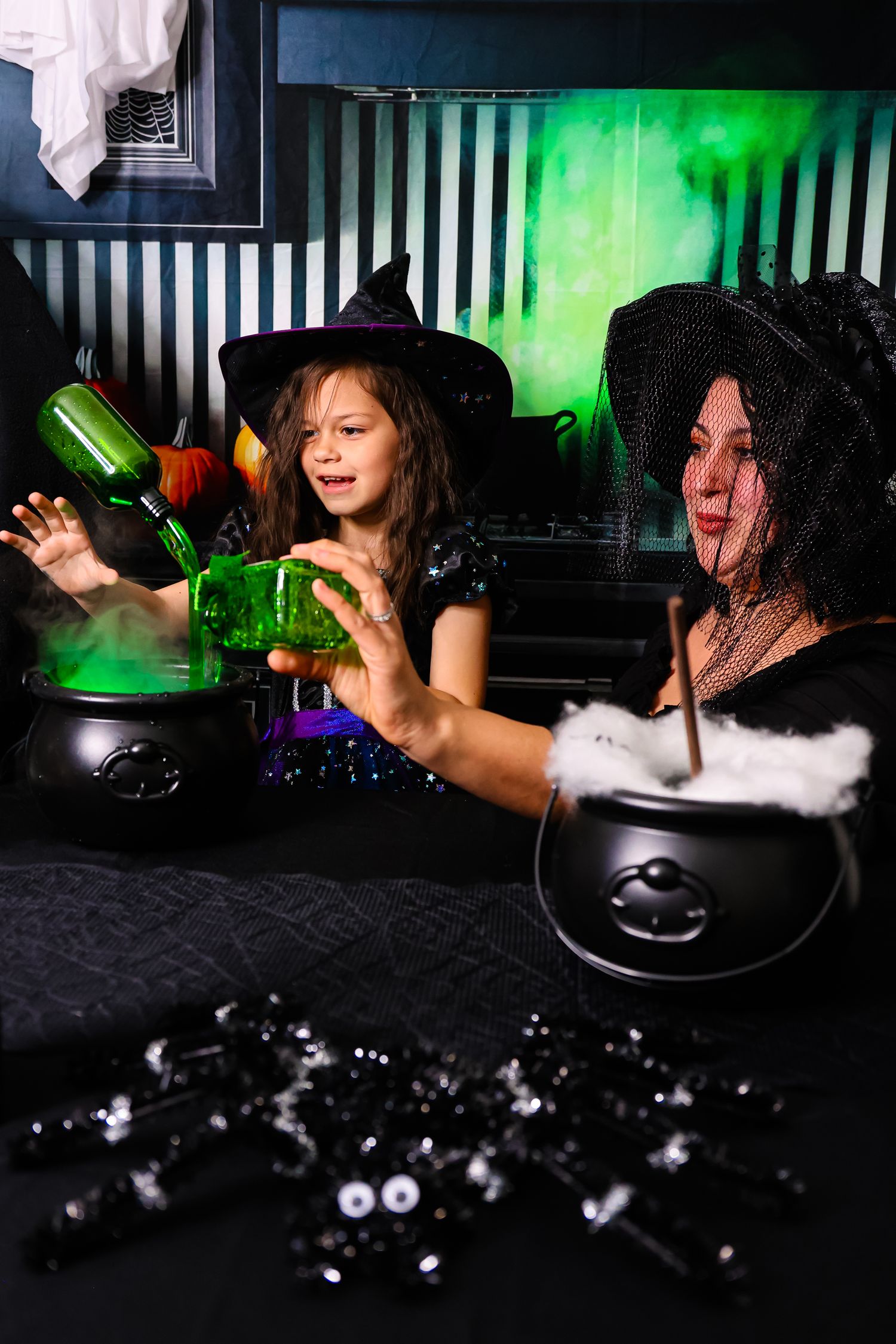 Two witches in black hats mix bubbling green potions in cauldrons for a spooky Halloween scene.