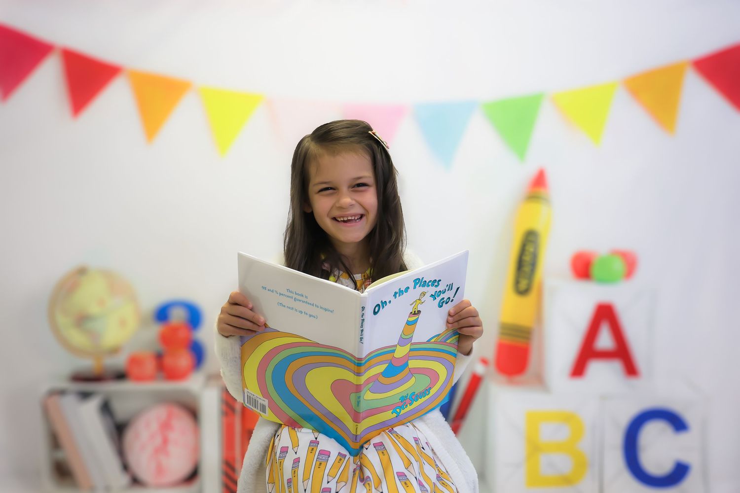 A person reads a colorful children's book in a classroom decorated with alphabet letters and festive bunting banners.