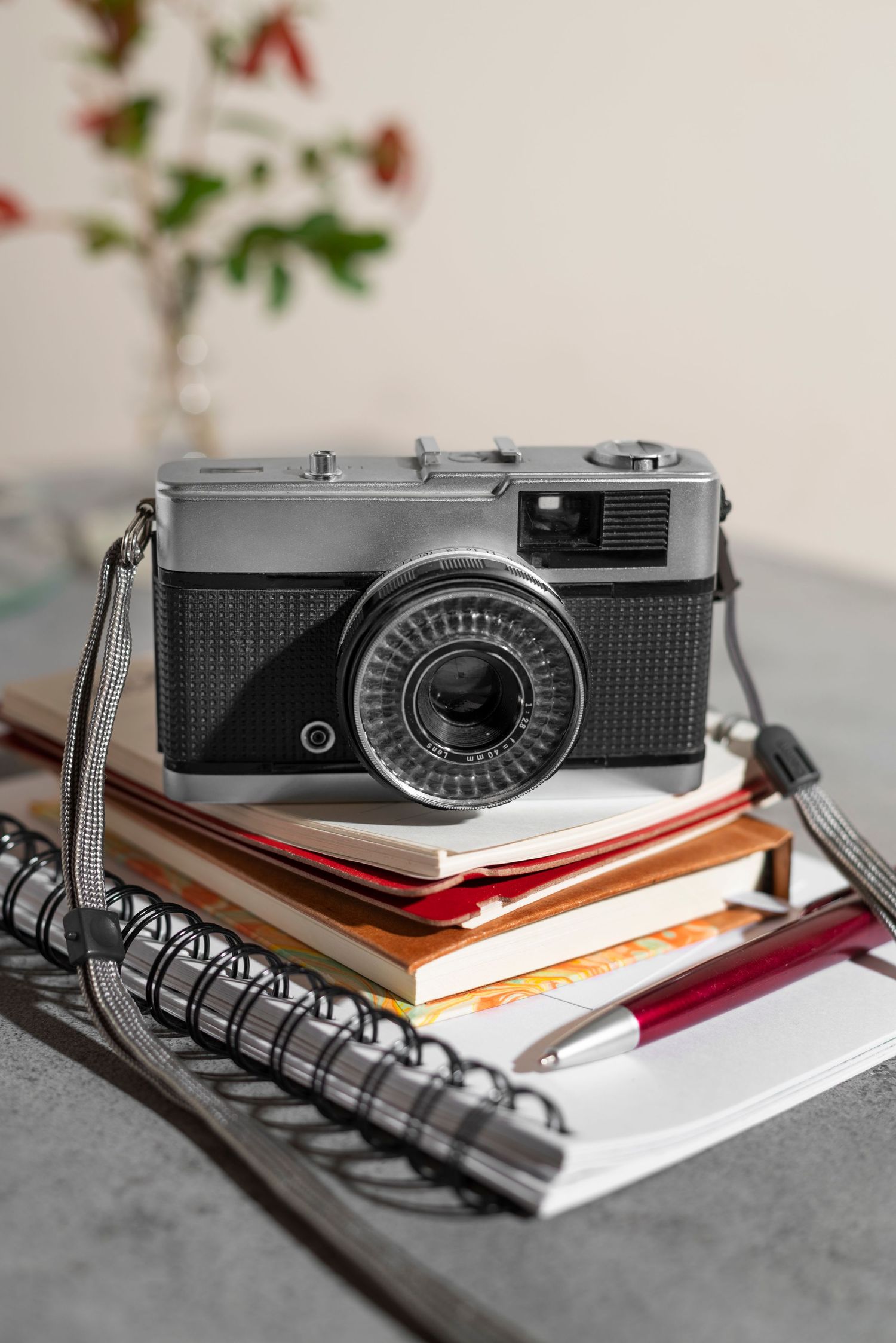 Vintage film camera resting on stack of colorful notebooks with spiral binding and pen on gray surface.