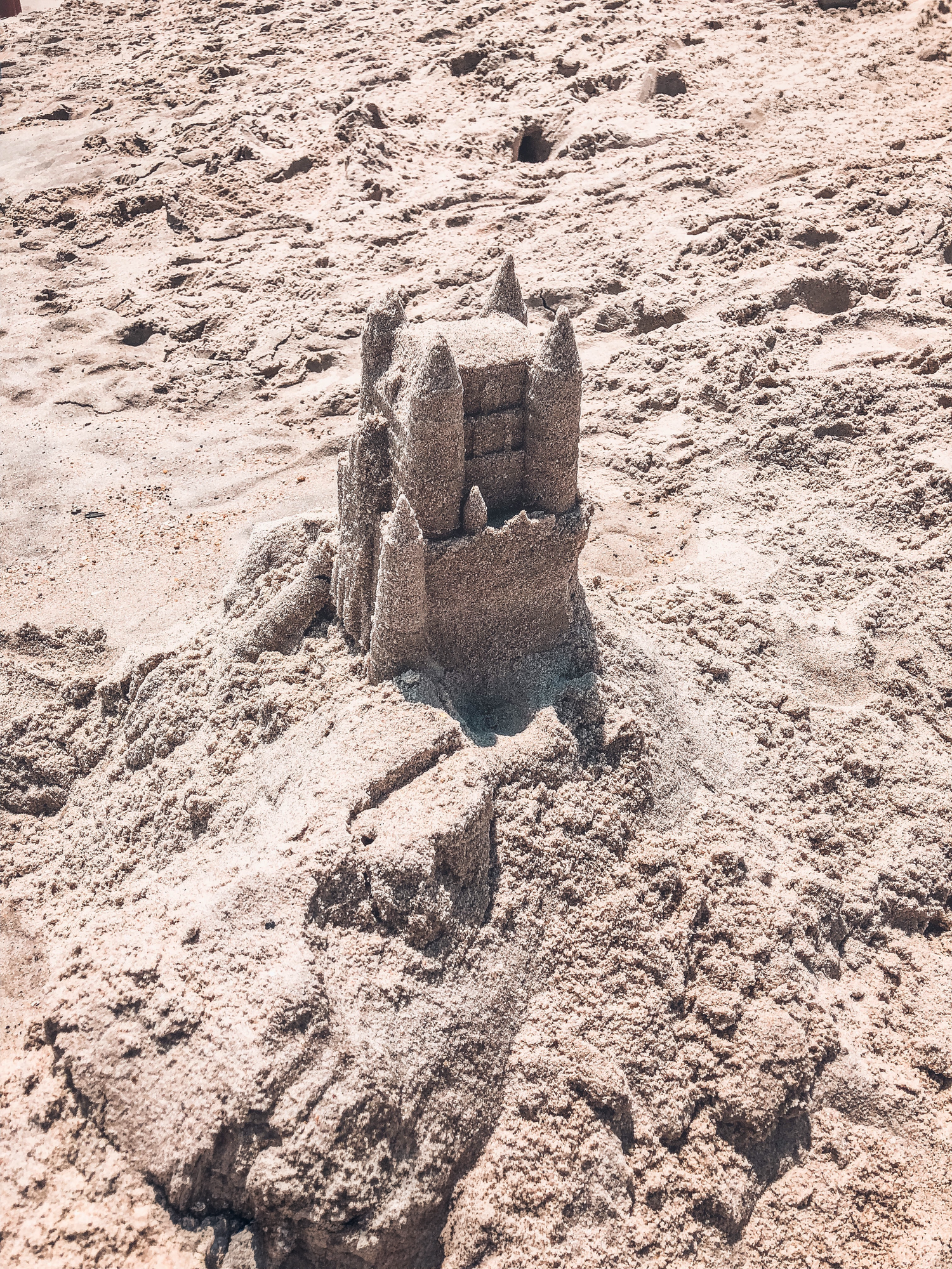 A detailed sandcastle with towers and battlements built on a sandy beach on a sunny day.