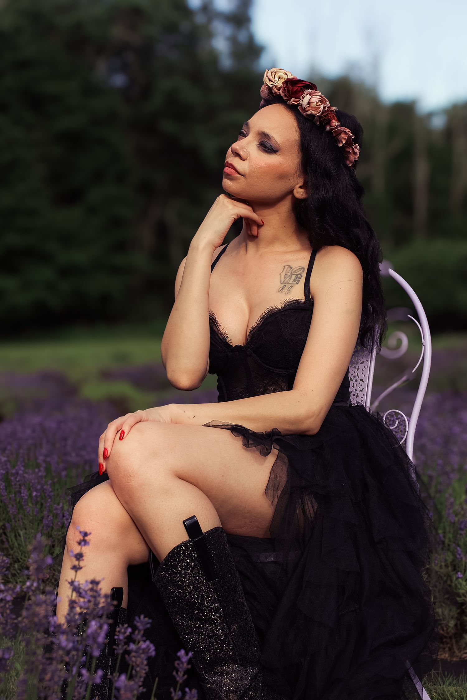 Artistic portrait of someone posing in a black dress among blooming purple lavender flowers at sunset.