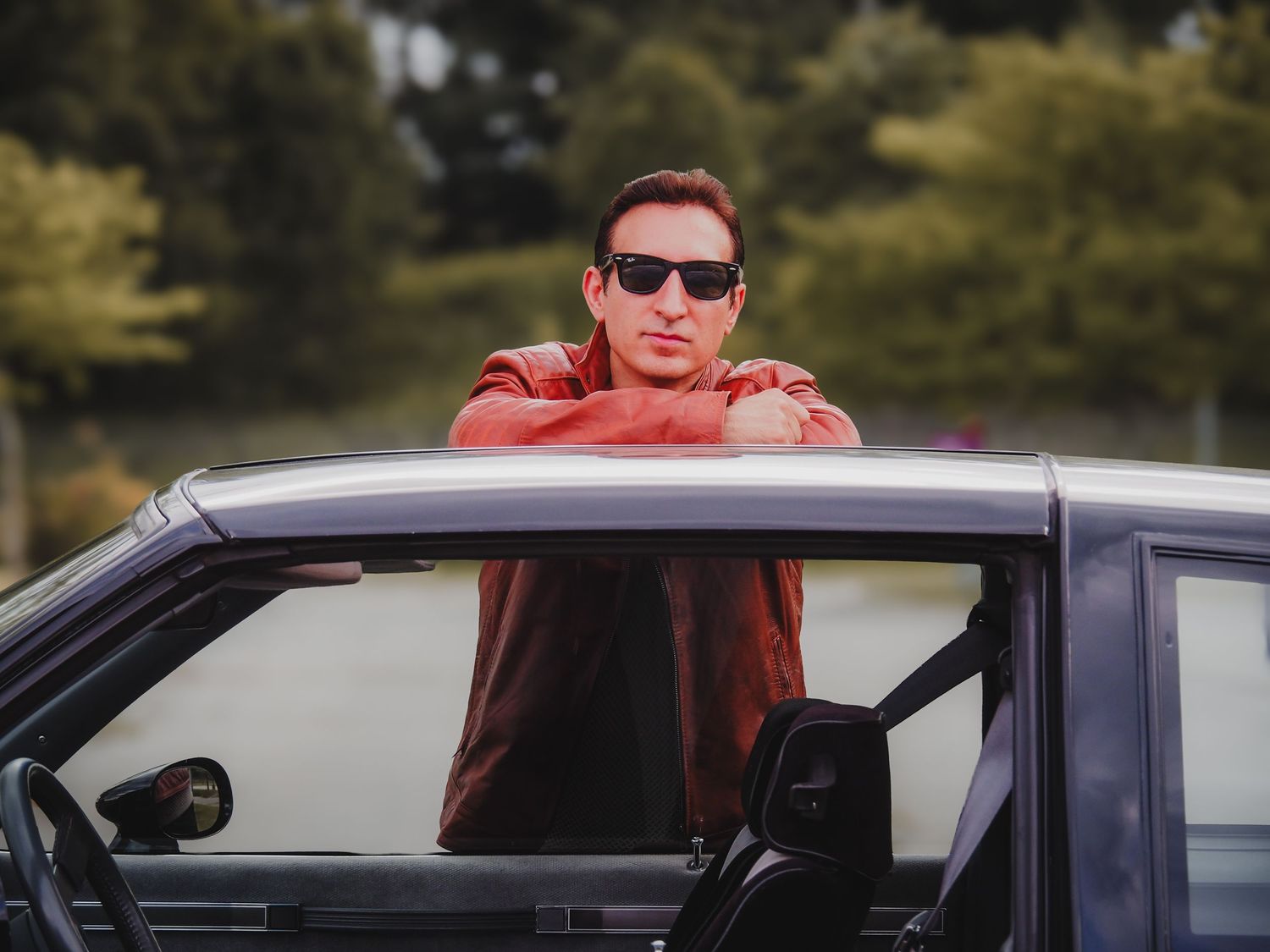 A person in a red hoodie drives a black car on a sunny day.