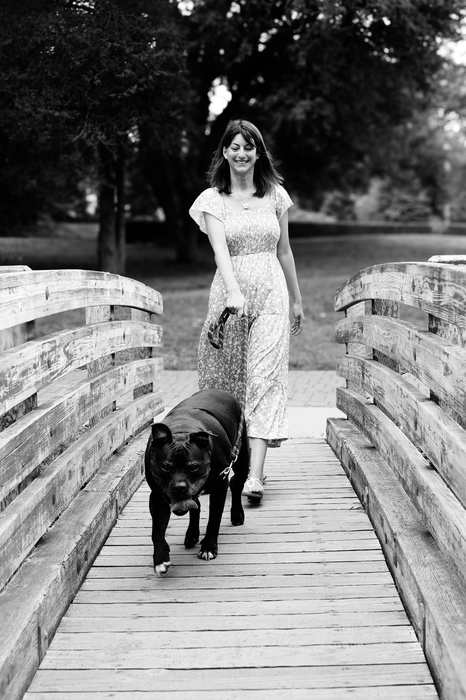 A sequence of black and white photos shows a person in a dress walking across a wooden bridge with a black dog.