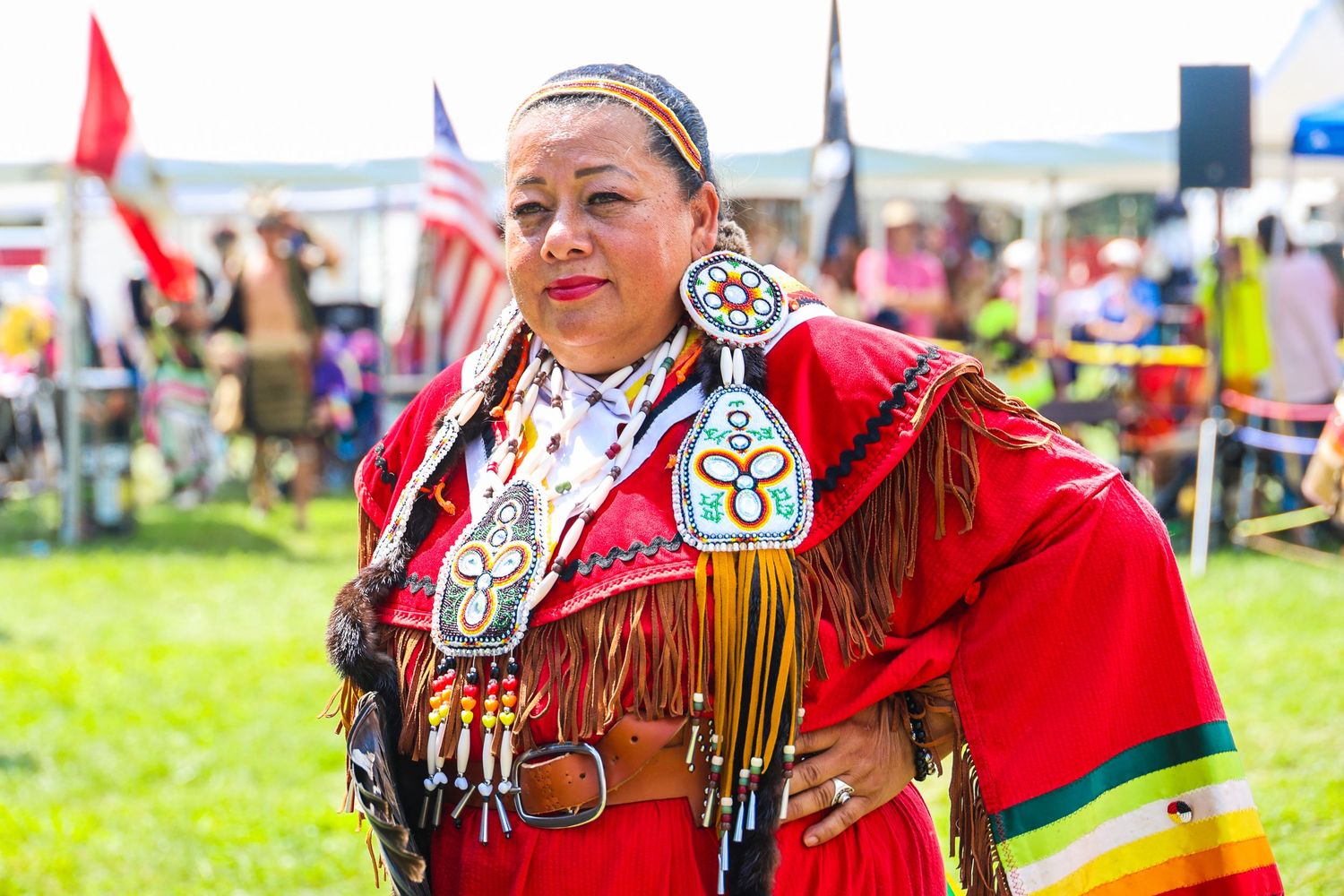 Native American dancers in vibrant red regalia perform traditional dances at an outdoor powwow celebration.