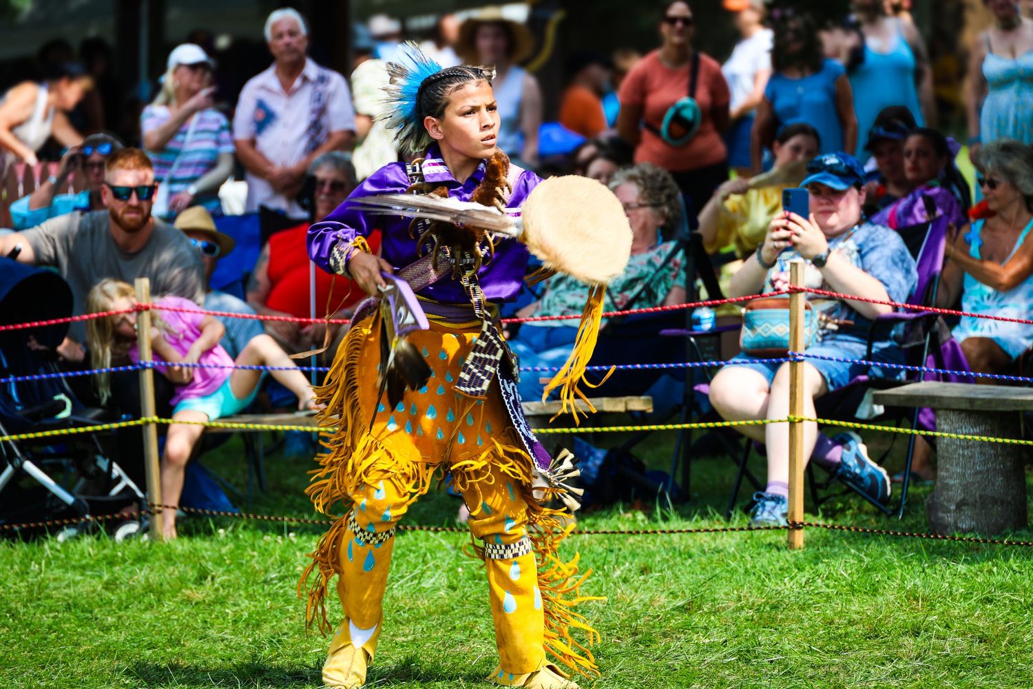 Native American dancers perform traditional dances in colorful regalia at an outdoor powwow celebration.