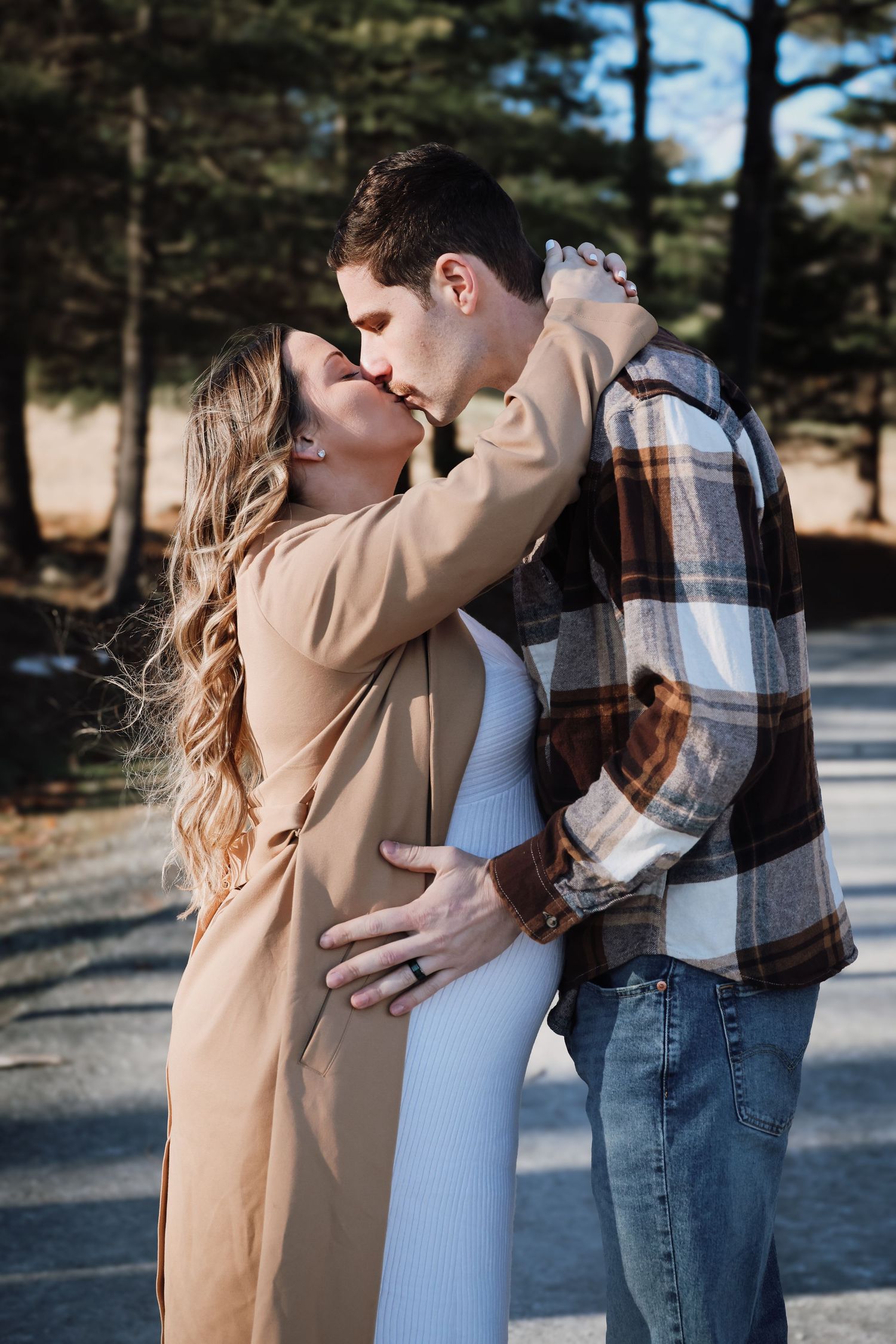 A couple sharing tender moments in a winter outdoor setting wearing casual clothing and a tan coat.