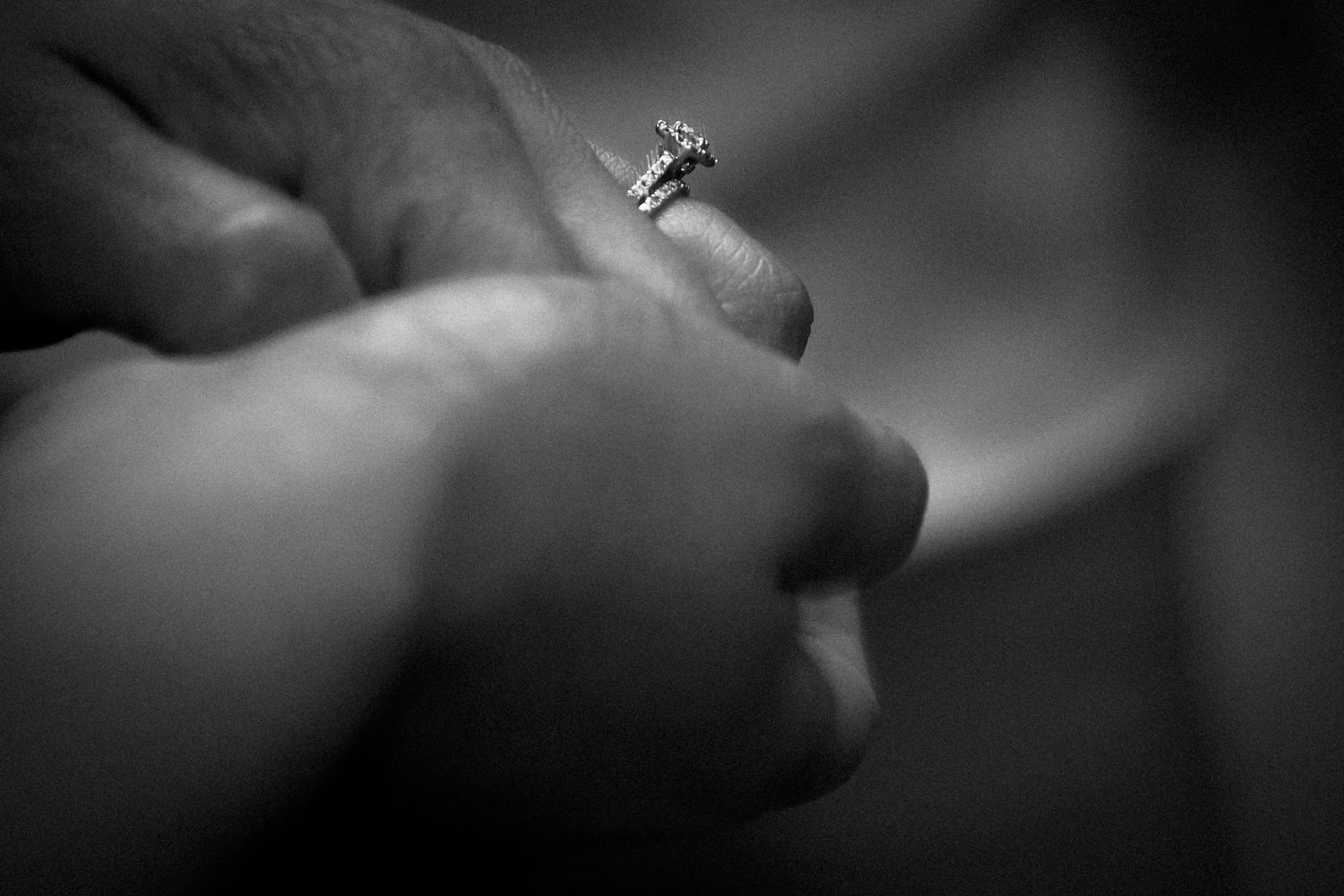 Close-up black and white photo of a hand holding an engagement ring with a sparkling diamond solitaire.
