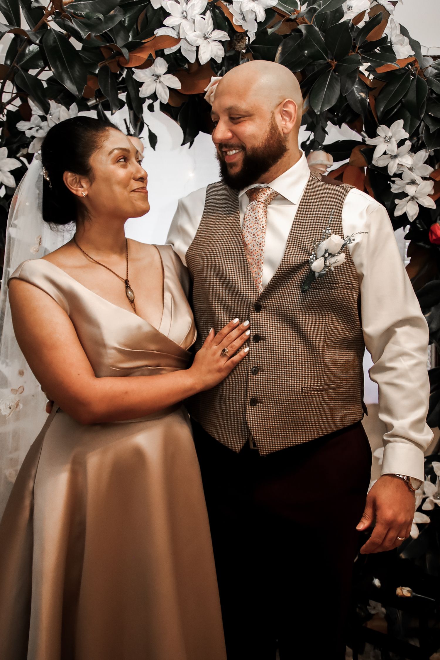 A couple shares tender moments in formal attire against a backdrop of white flowers.