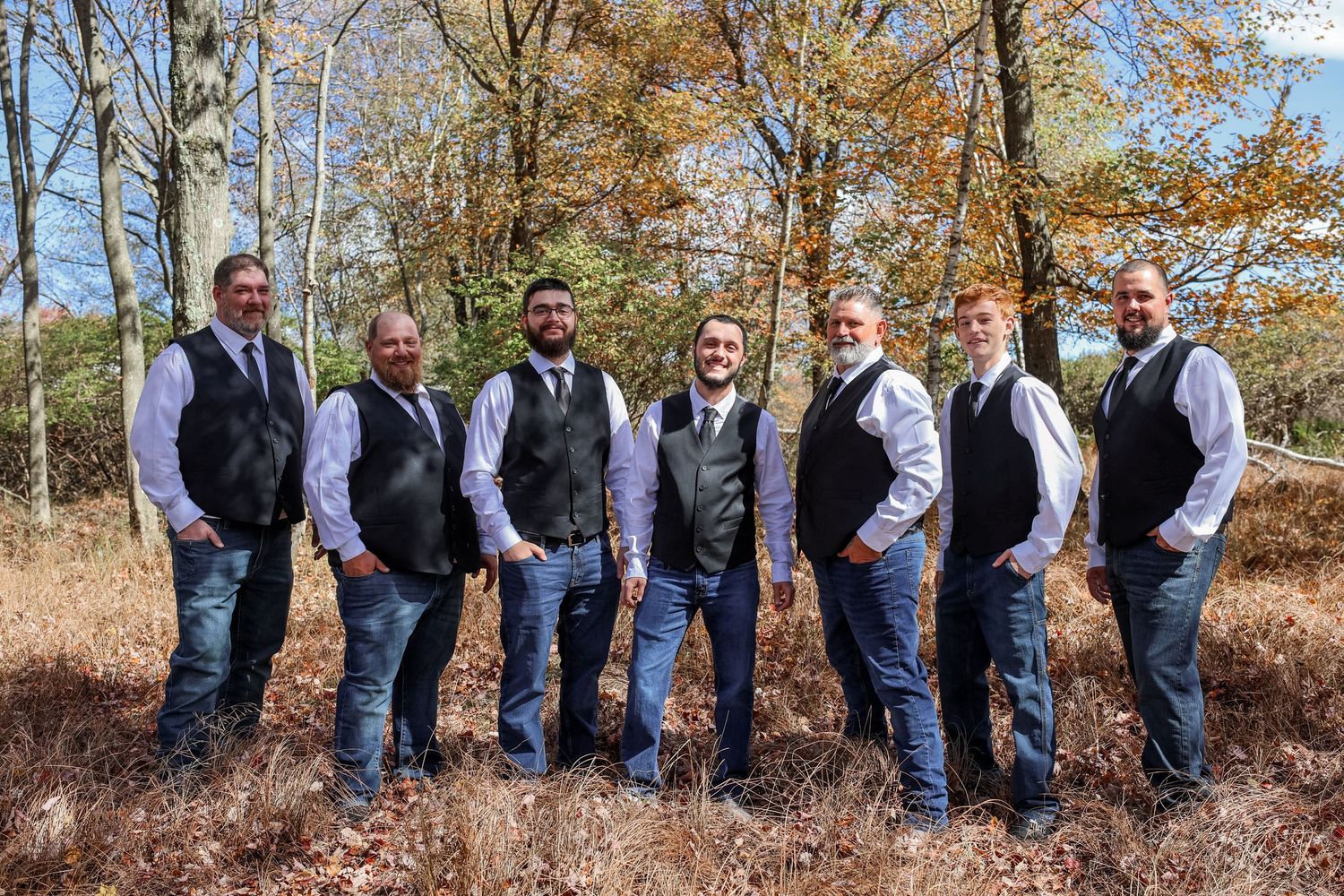 A group of people in matching attire stand in a line among autumn trees during a formal outdoor event.