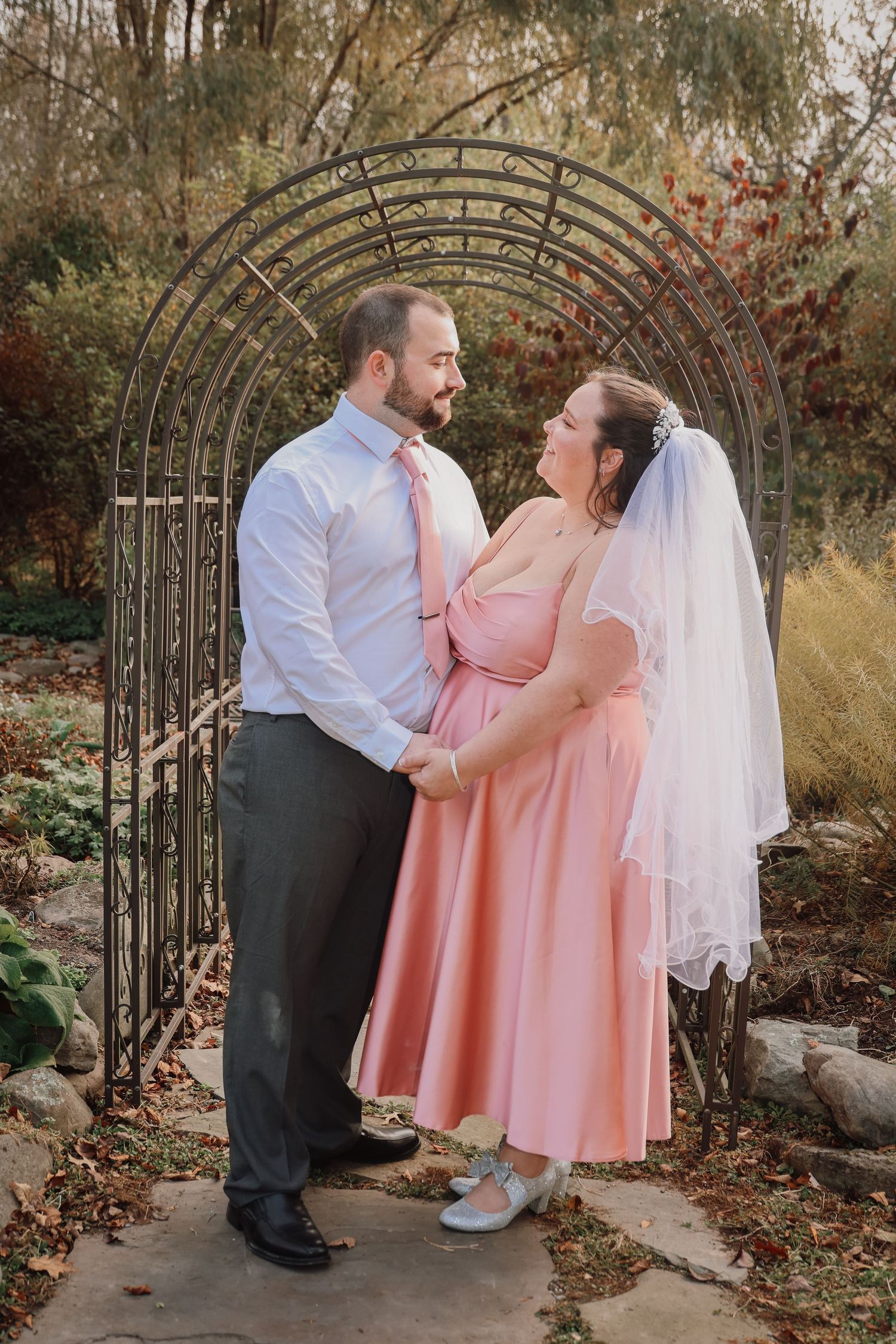 A couple in wedding attire shares tender moments under a garden archway in a series of romantic autumn photos.