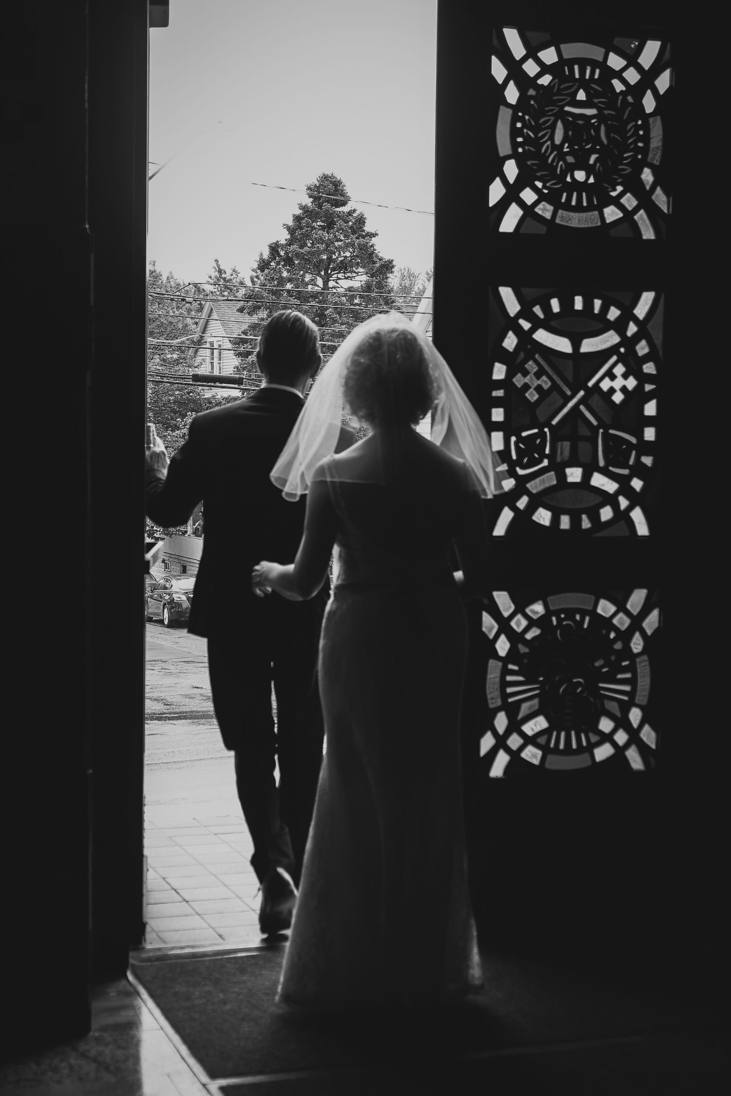 Silhouetted figures stand in doorways with decorative patterns visible in black and white architectural photography.