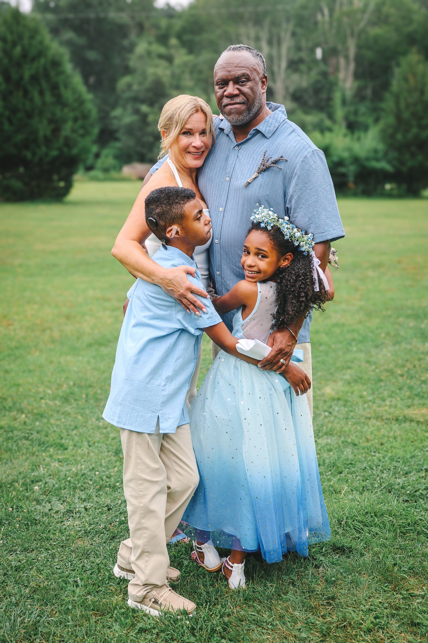 A family shares tender moments together in a green field while wearing coordinated light blue and khaki outfits.