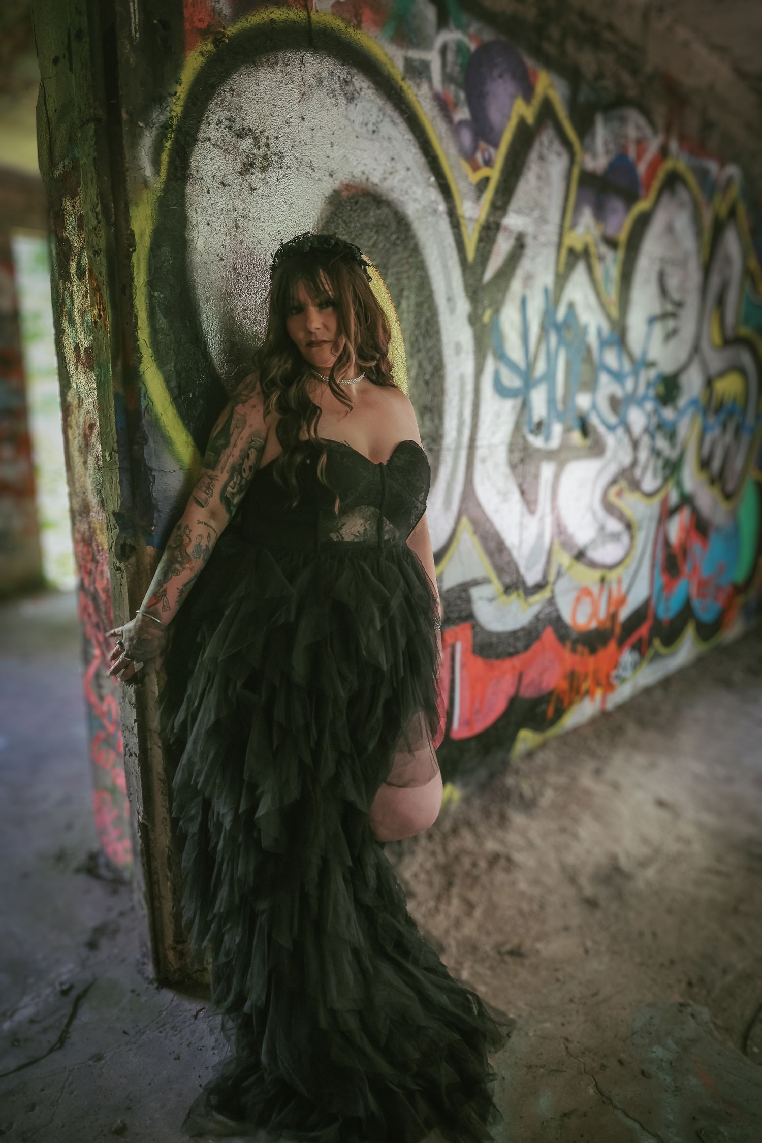 A dramatic gothic fashion photo with a black flowing dress against graffiti-covered walls in an urban setting.