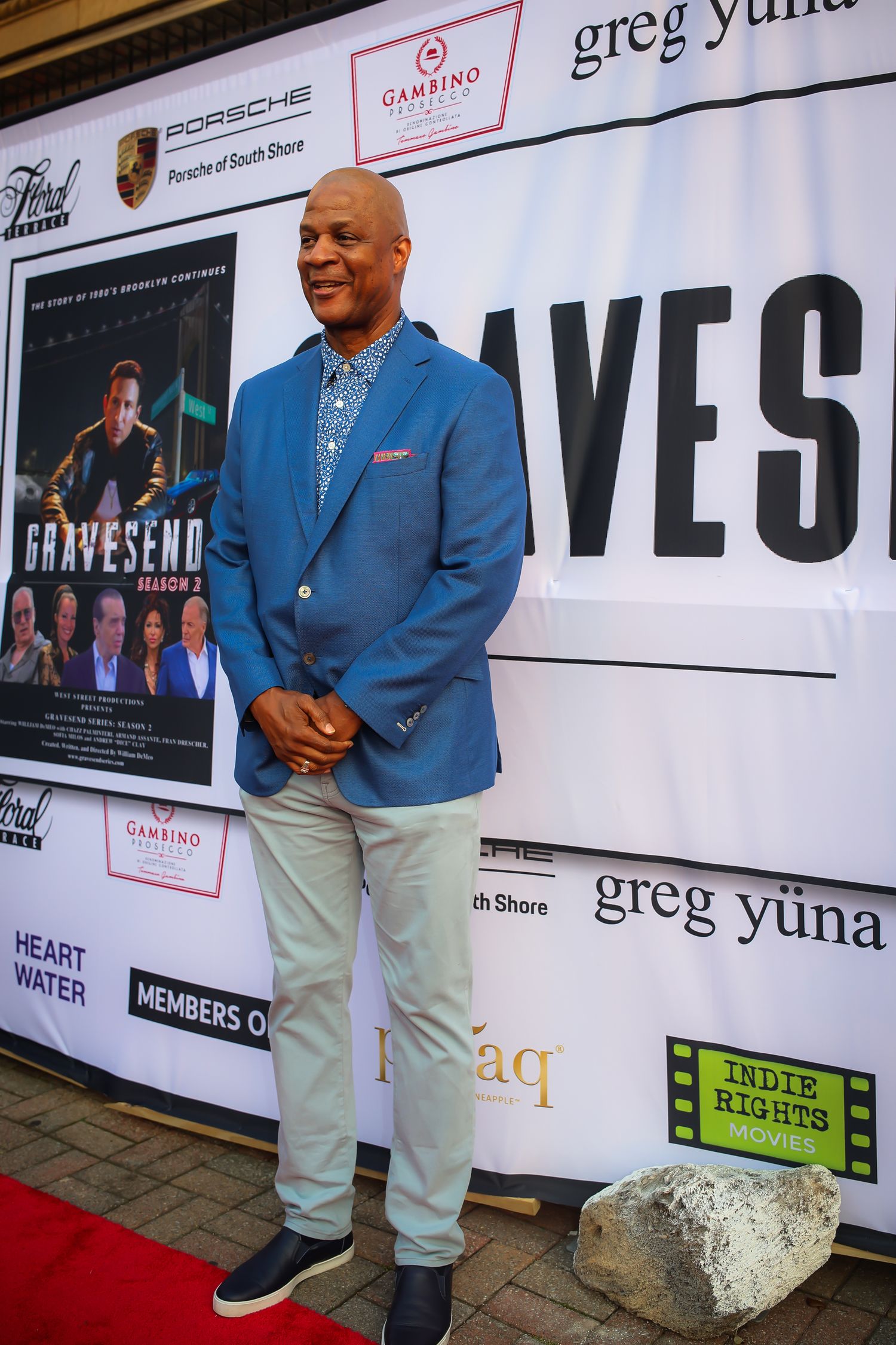 A person wearing a bright blue blazer and light khakis poses on a red carpet at a media event.