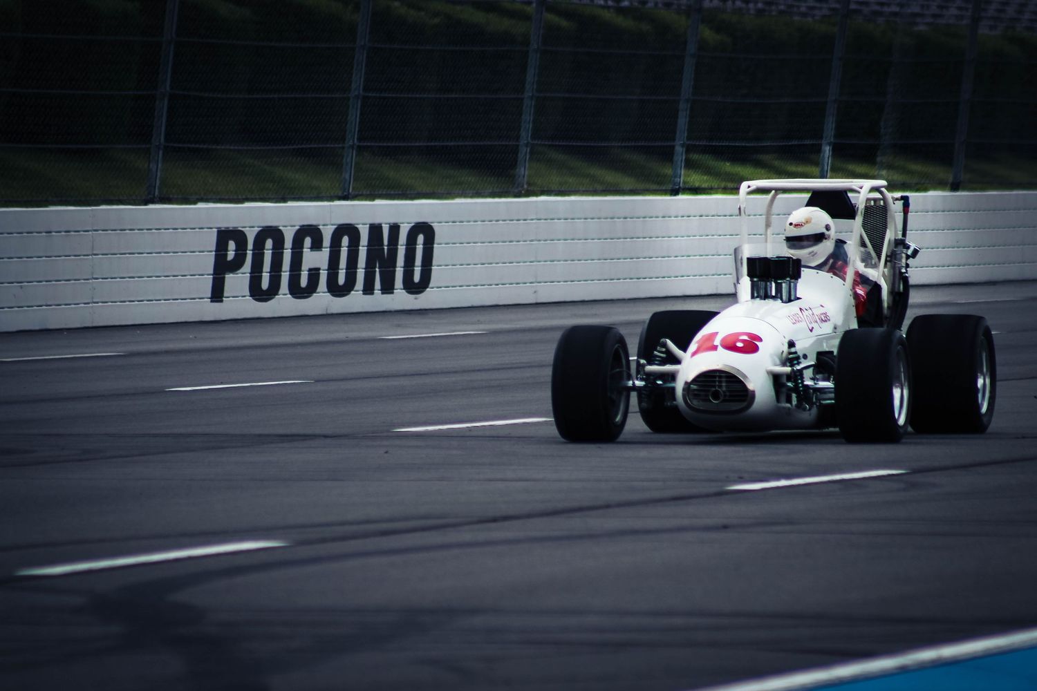 Race car speeds around a corner at Pocono Raceway during a competitive motorsport event.