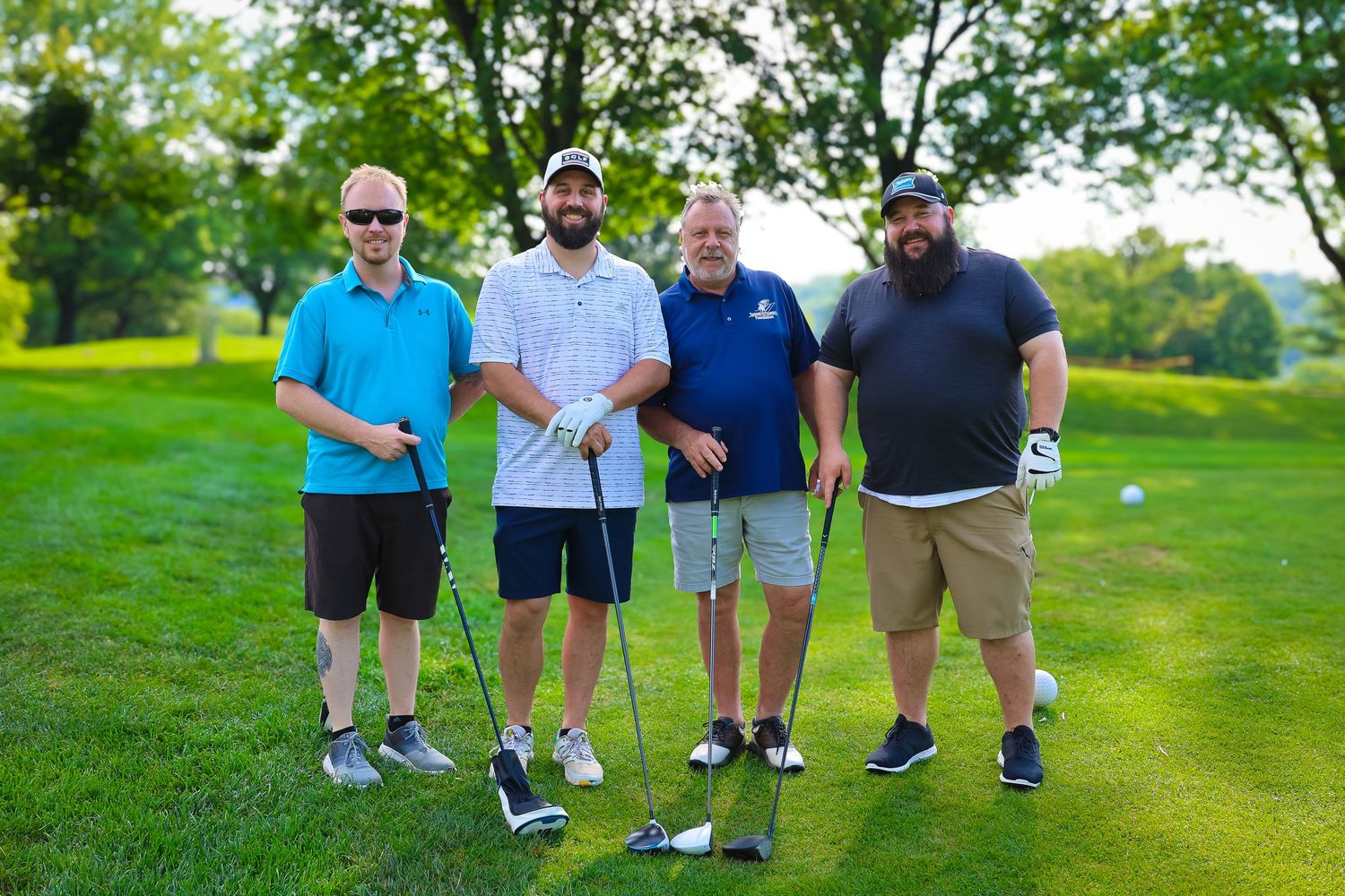 A group of golfers stand together on a lush green golf course fairway during a sunny day.