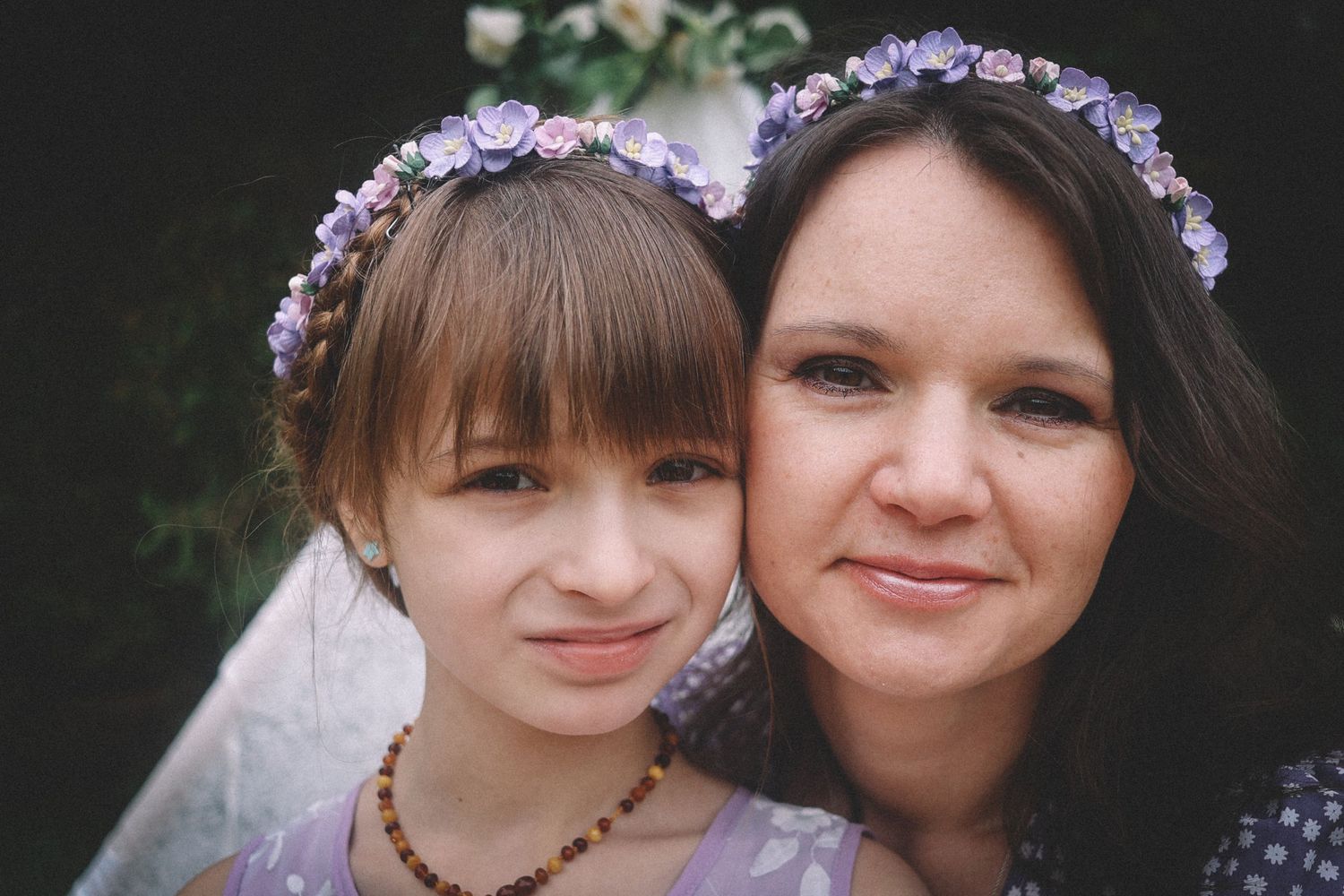 A mother and daughter wearing matching purple flower crowns smile together in a series of black and white photos.
