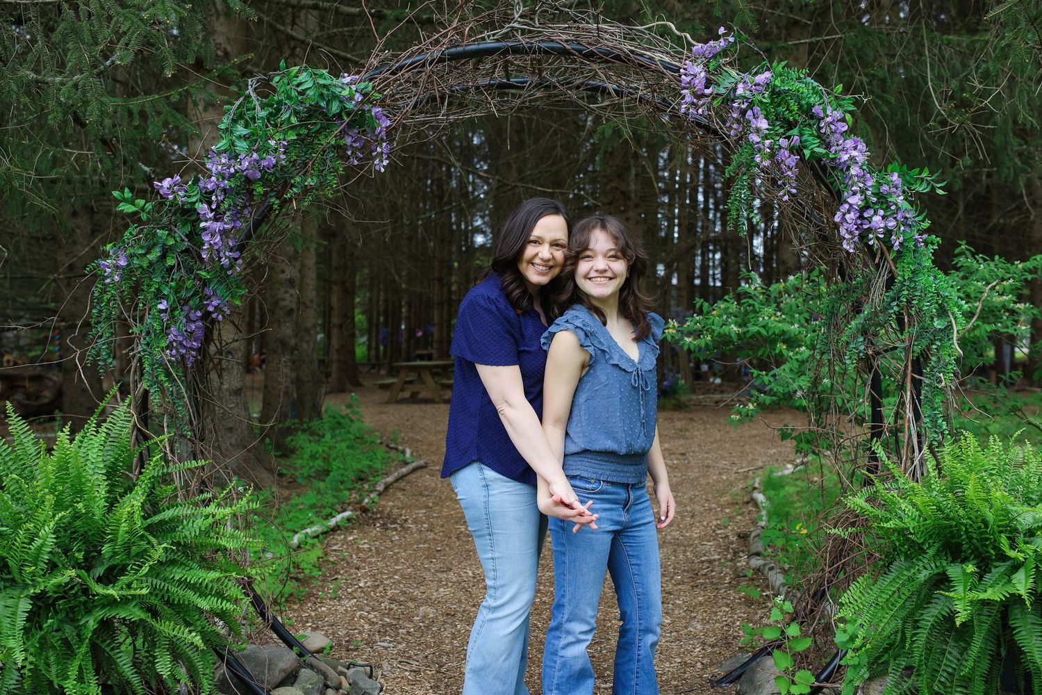A couple poses together in a lush green forest setting with purple wildflowers in the background.