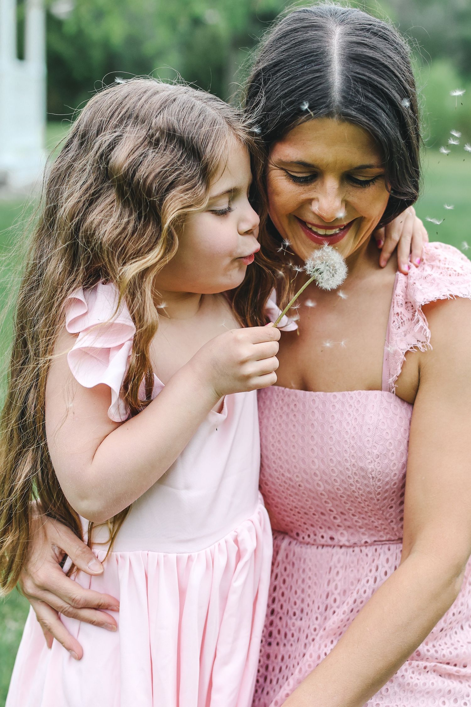 A tender moment between a child and woman wearing matching pink dresses in a garden setting.