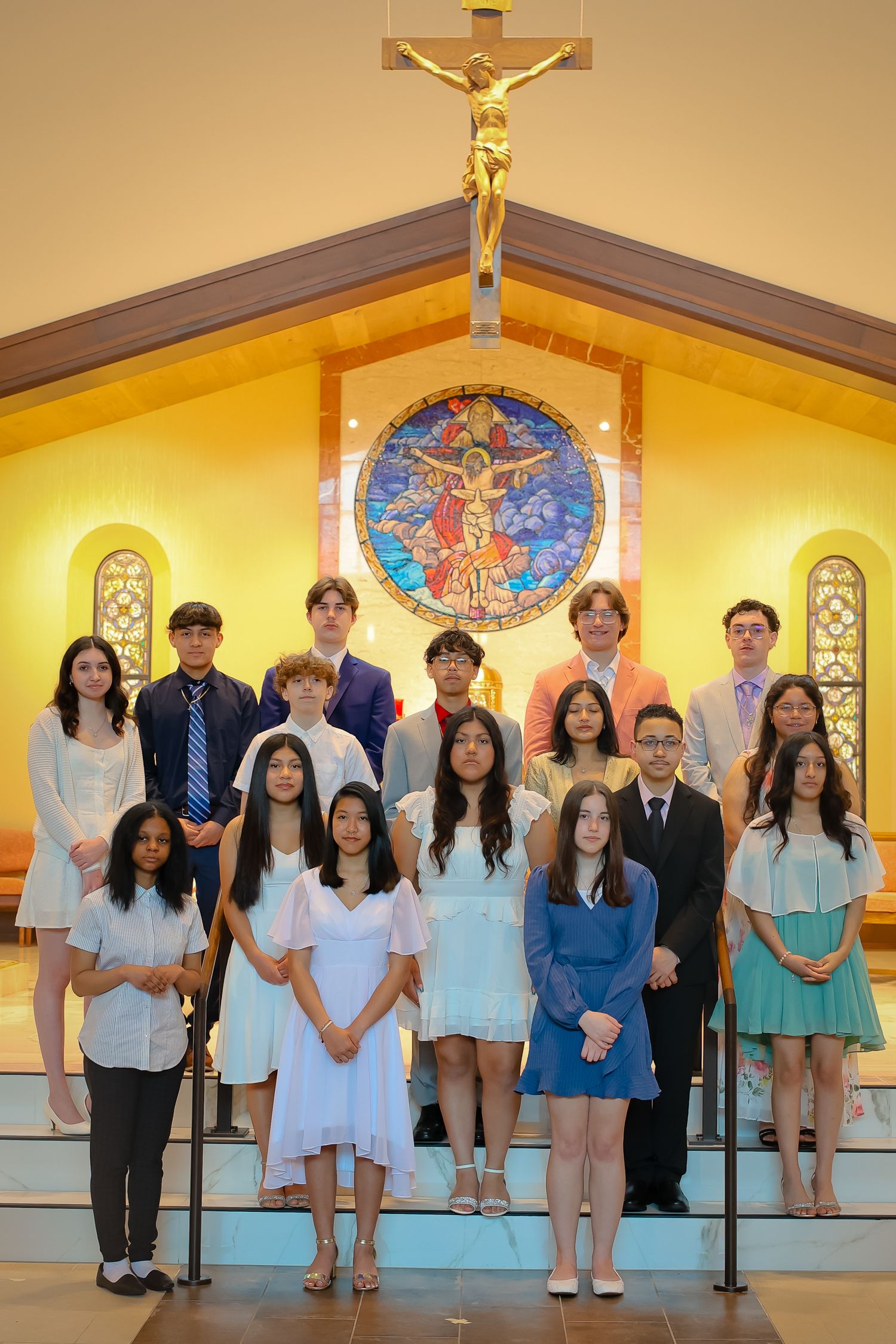 A group of people standing together in a church or chapel with religious artwork and a crucifix visible in the background.