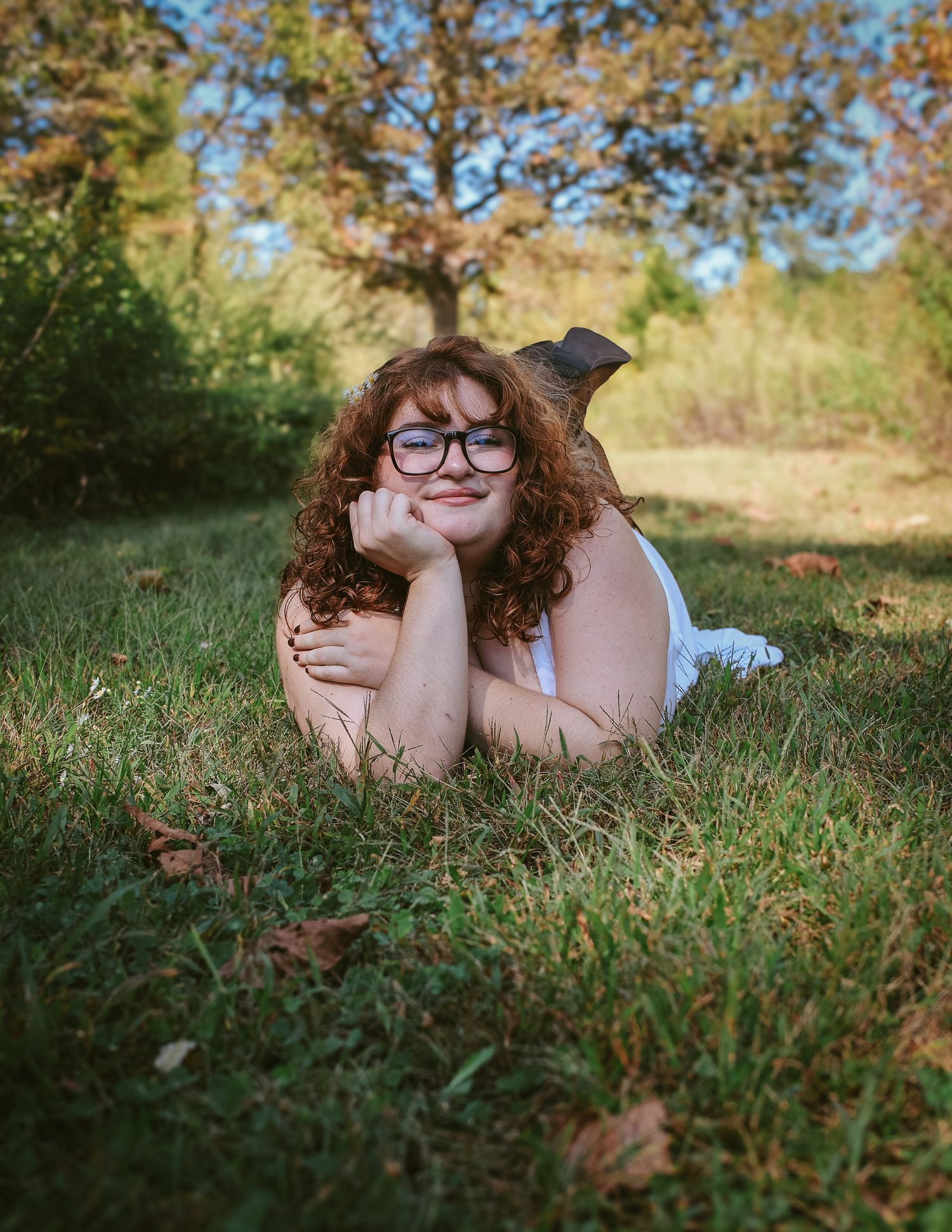 A person wearing glasses lies on green grass in a natural outdoor setting during autumn.