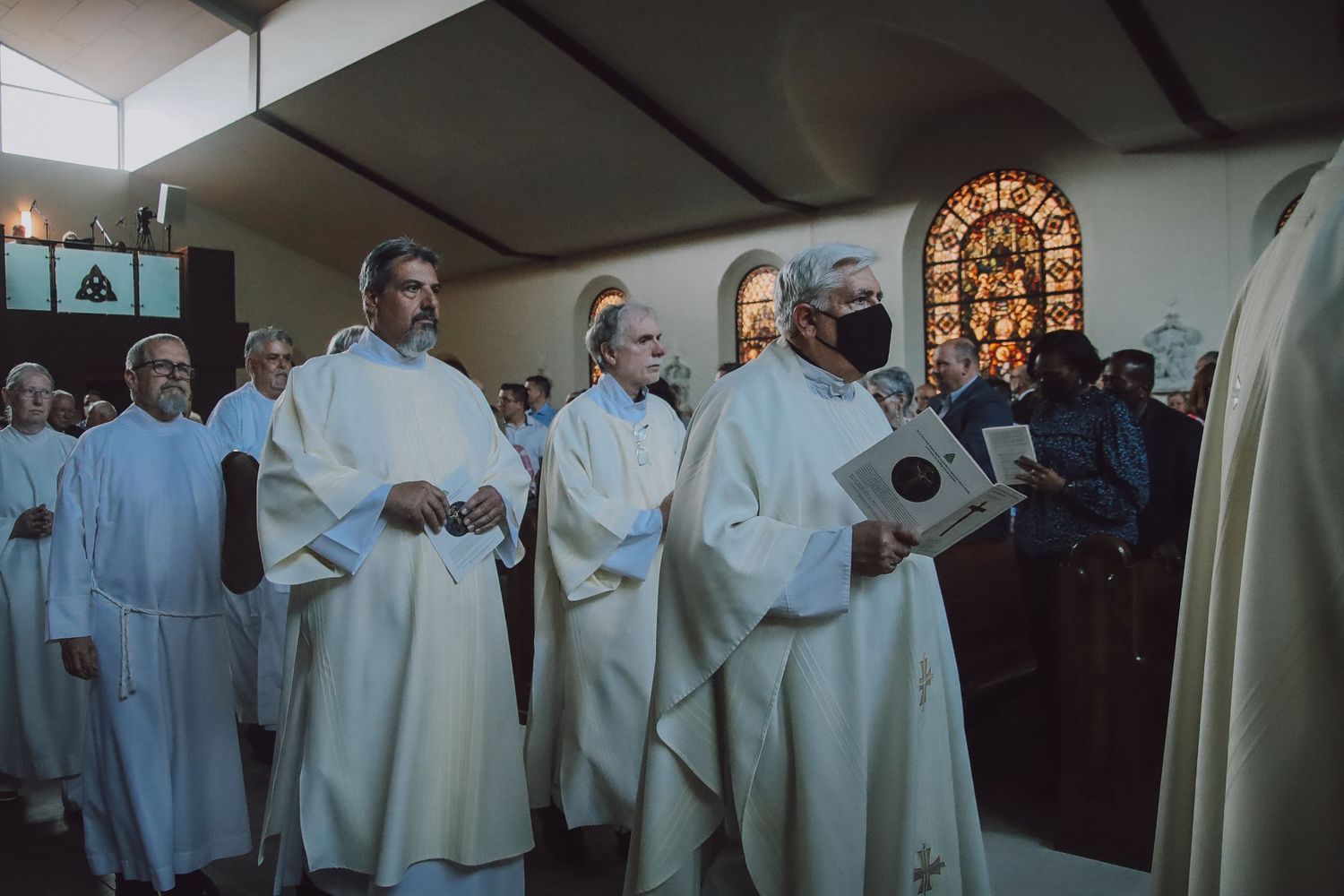 Religious clergy members in white robes gather during a ceremonial service in a church setting.