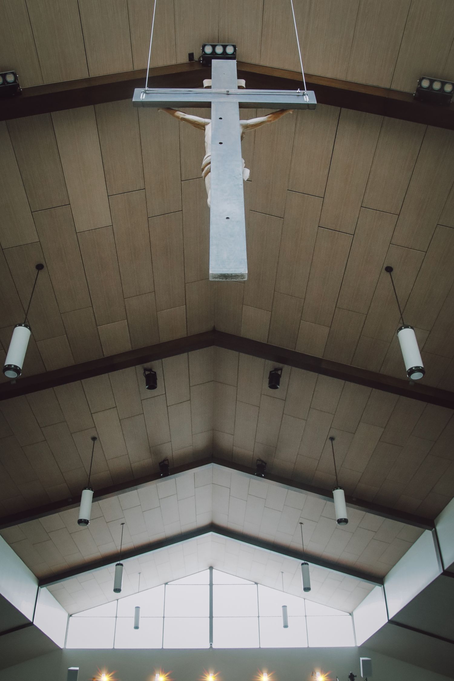Geometric white ceiling with exposed wooden beams and pendant lights creates an angular architectural pattern in modern interior.