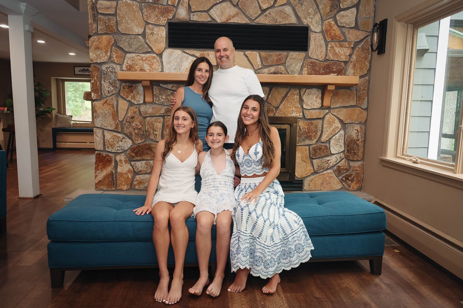 Family of five posing together on a blue couch in front of a stone fireplace in a cozy living room.