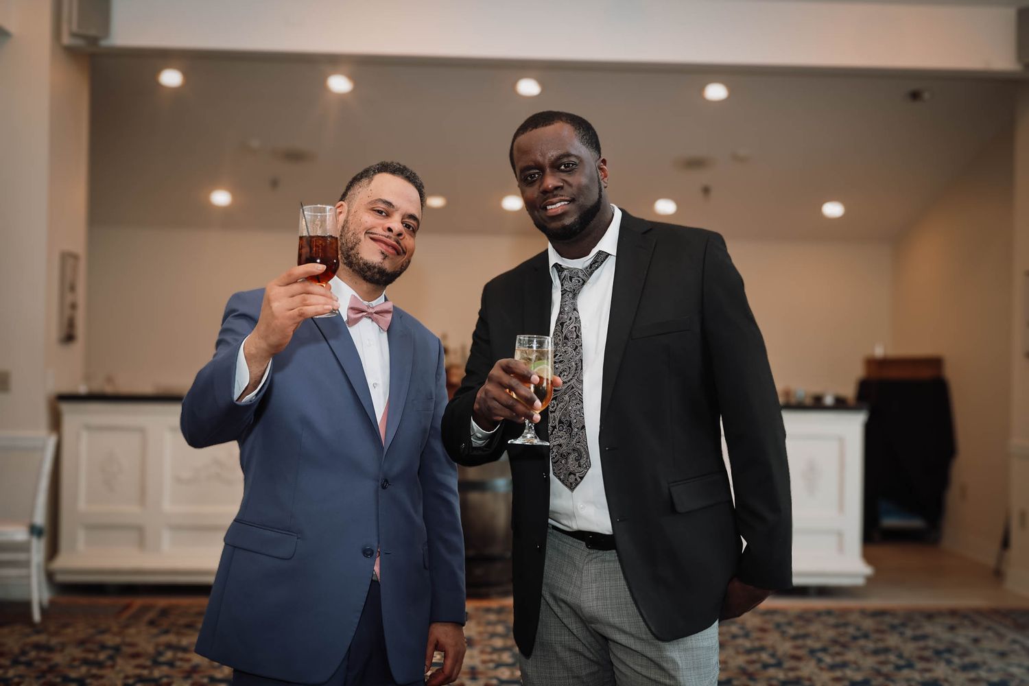 Two men in suits toasting with drinks at a formal event, smiling at the camera.
