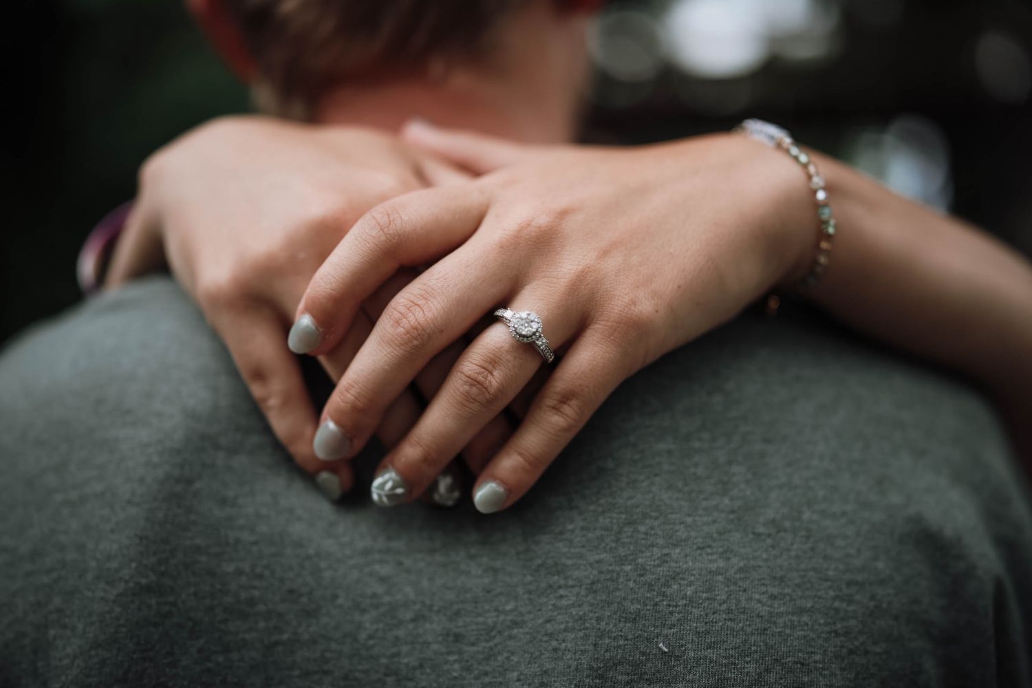 Close-up of a woman's hand with an engagement ring and bracelet resting on a man's shoulder.