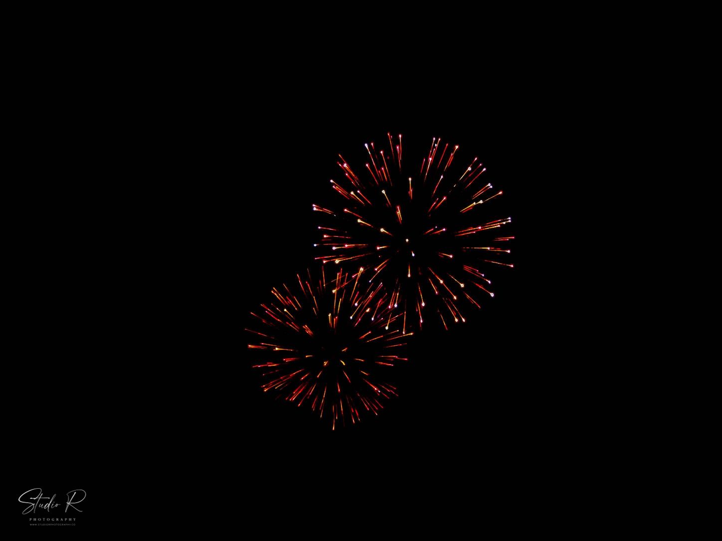 Two red fireworks bursting against a dark night sky in a vibrant Fourth of July celebration display.