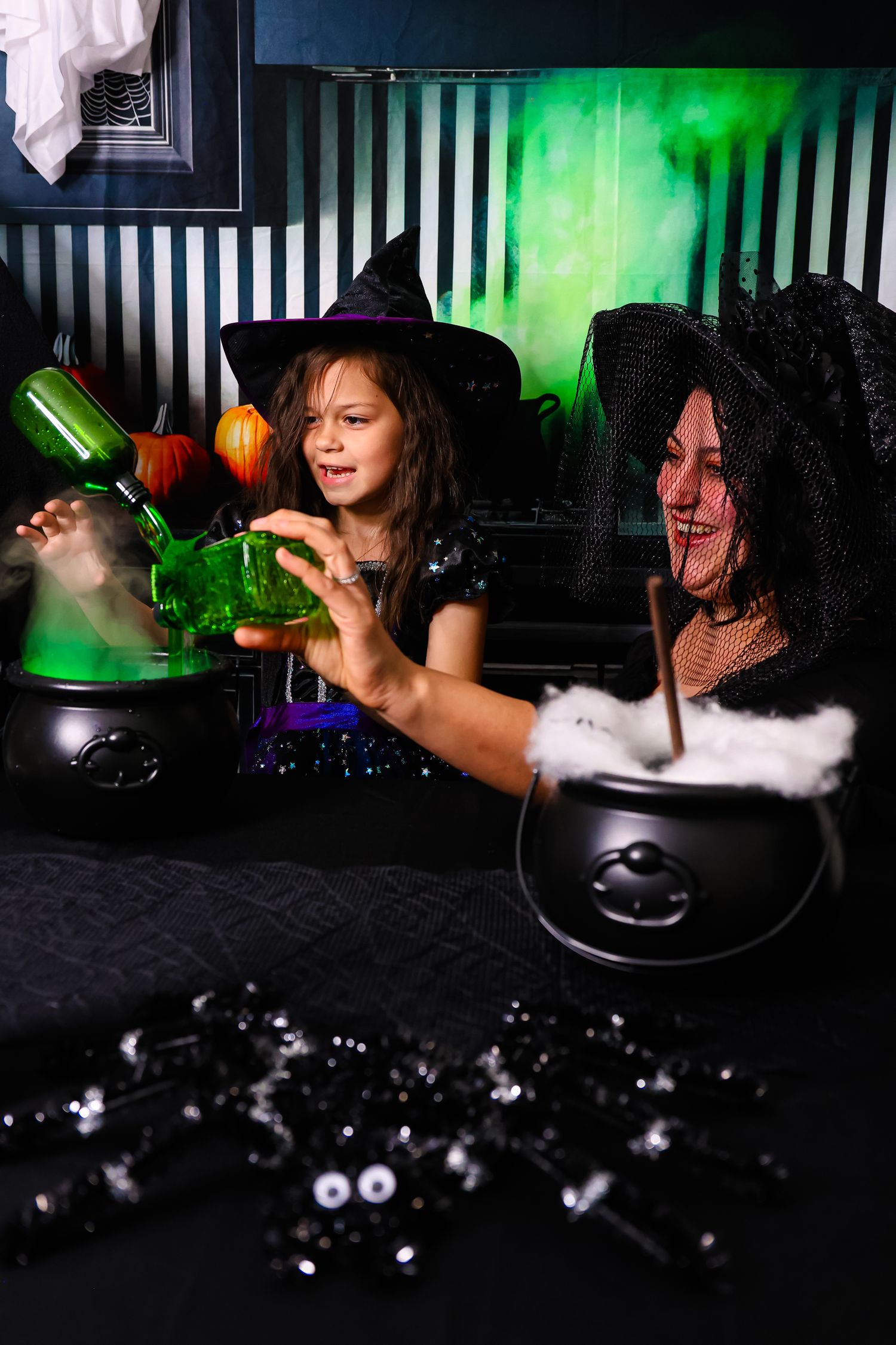 Two girls in witch costumes brewing potions in cauldrons with green smoke for Halloween.