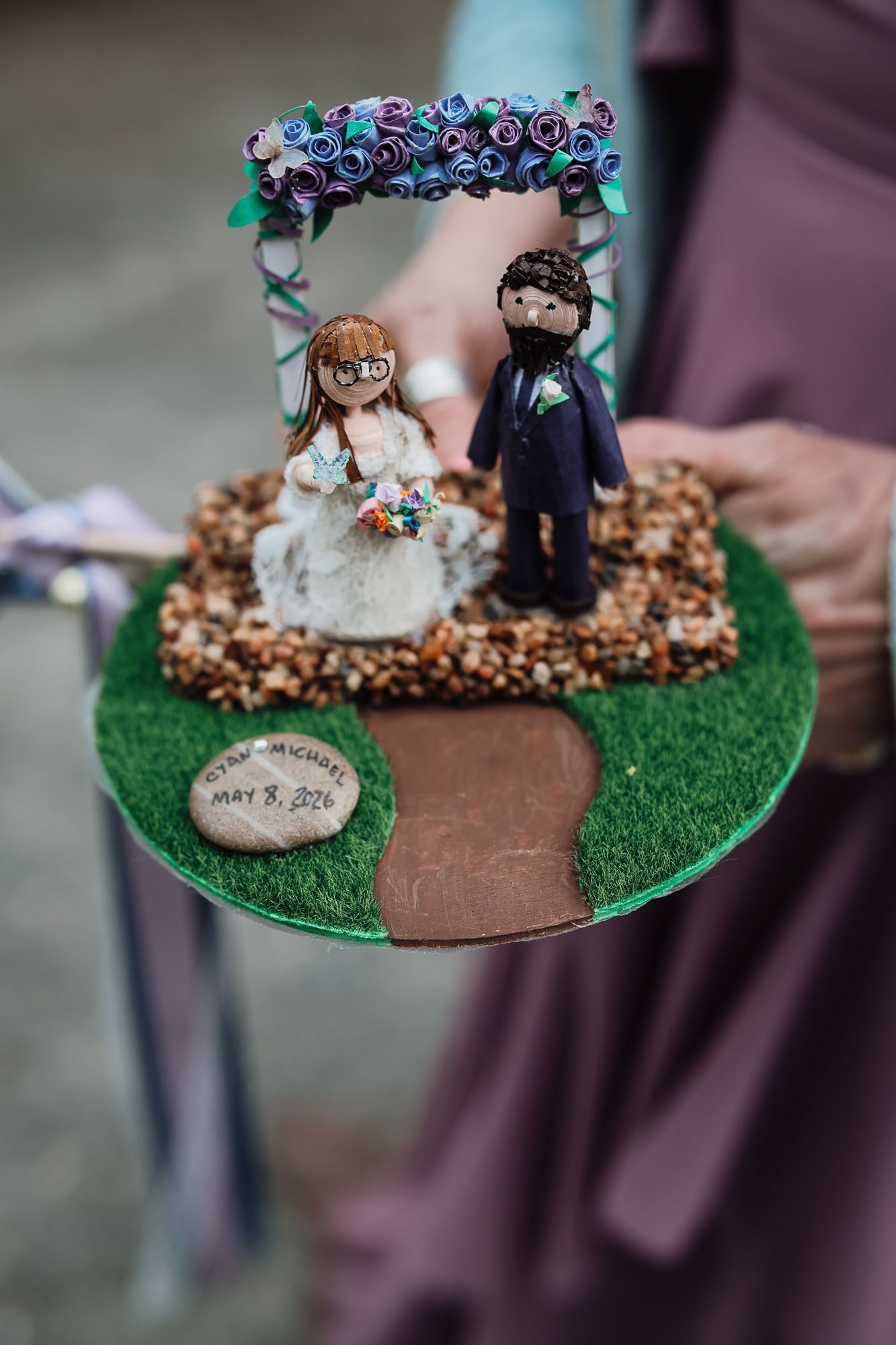 Custom wedding cake topper with bride and groom figurines under floral arch on green grass base dated May 18, 2024.