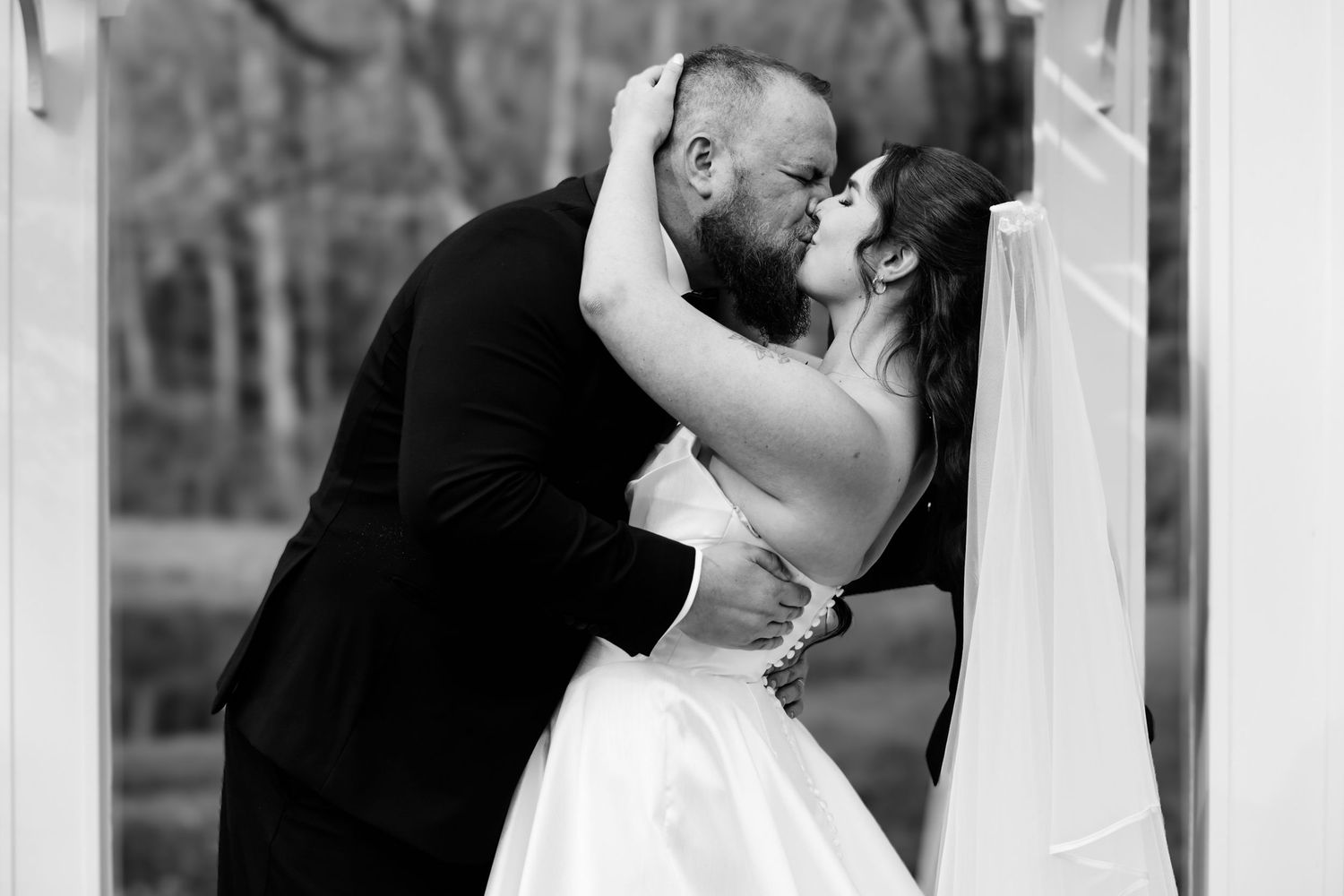 Black and white photo of a bride and groom sharing a romantic kiss on their wedding day.