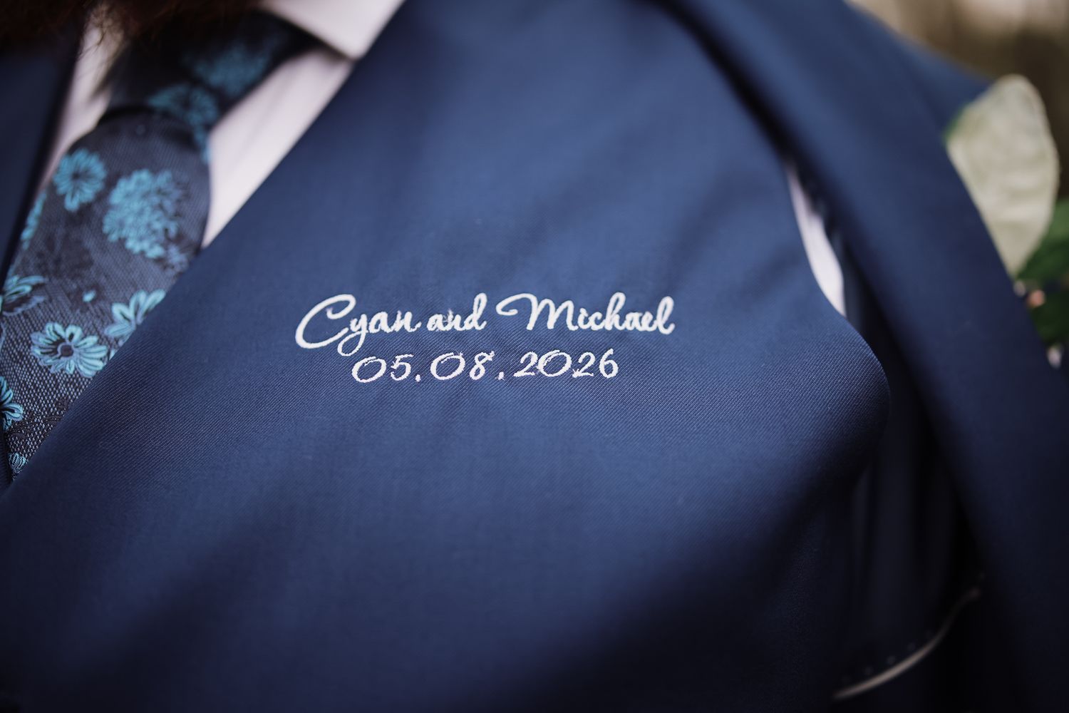 Navy suit jacket with embroidered wedding details reading Cyan and Michael 05.08.2026 in white script.
