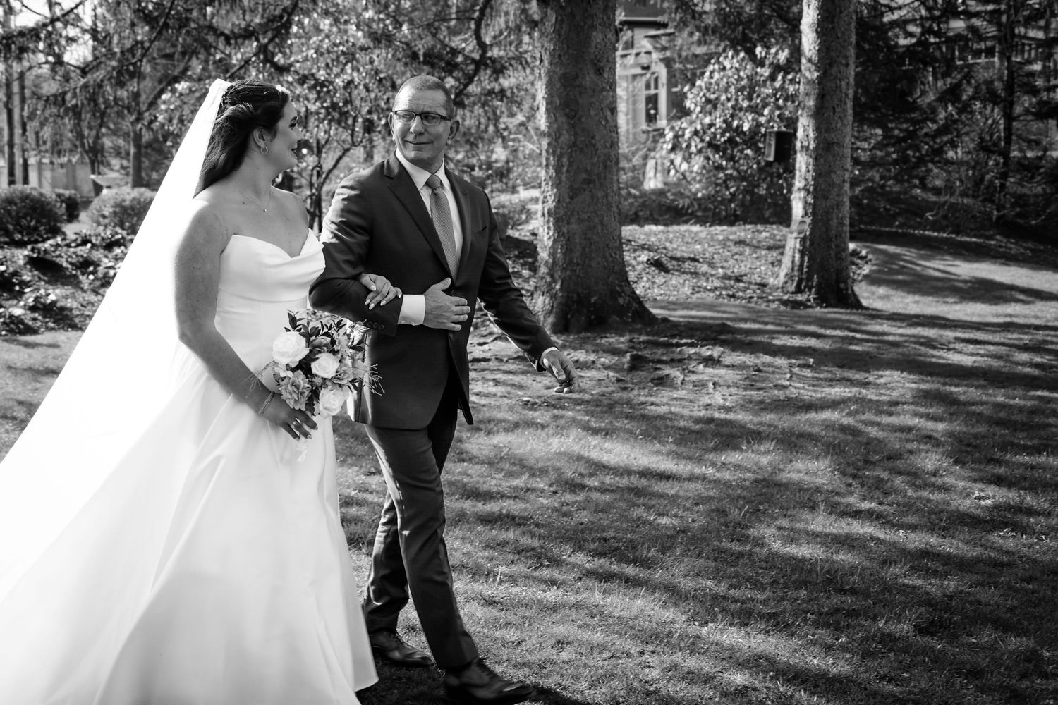 Black and white photo of a bride in a white gown and groom in a suit sharing a first look outdoors.