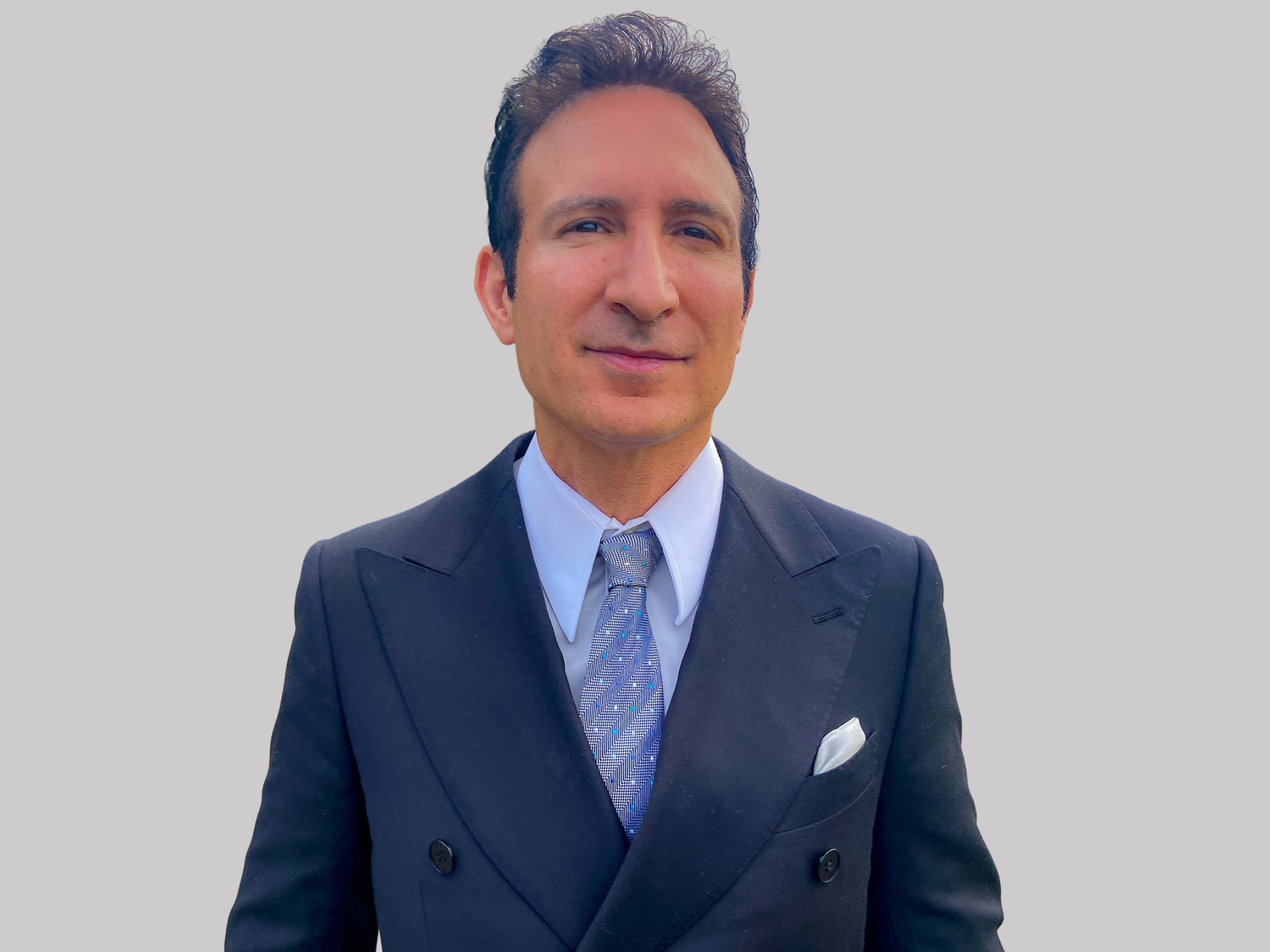 Professional wearing a navy blue suit and light blue tie poses for a series of headshots in a studio setting.