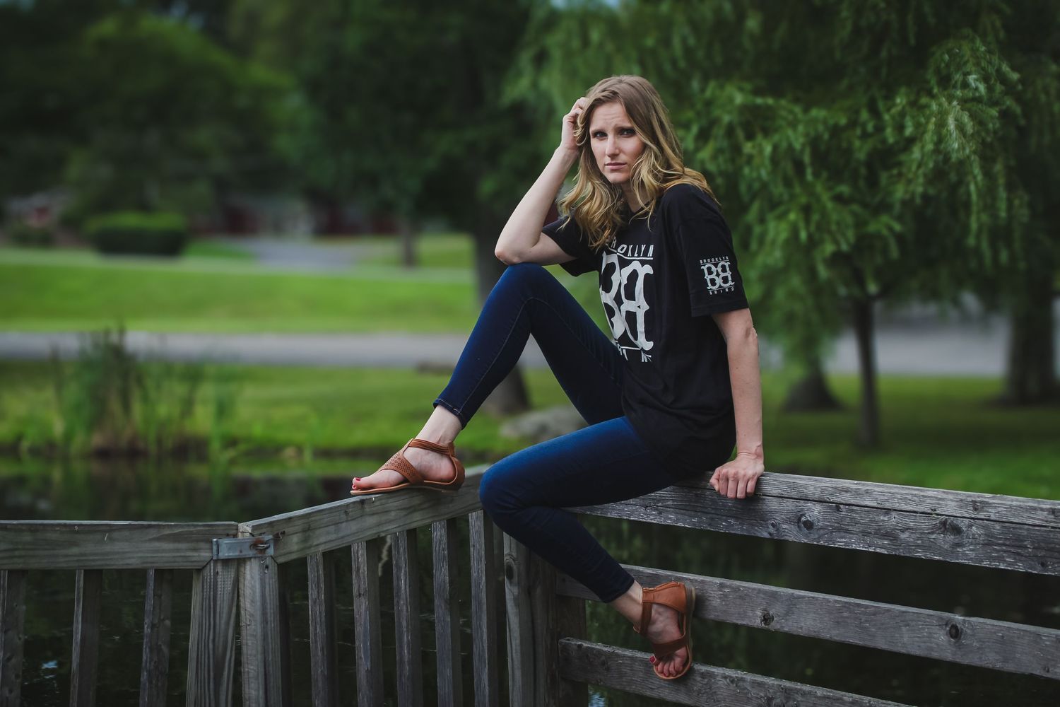 A senior portrait session in a park features artistic poses on a rustic wooden fence surrounded by lush greenery.