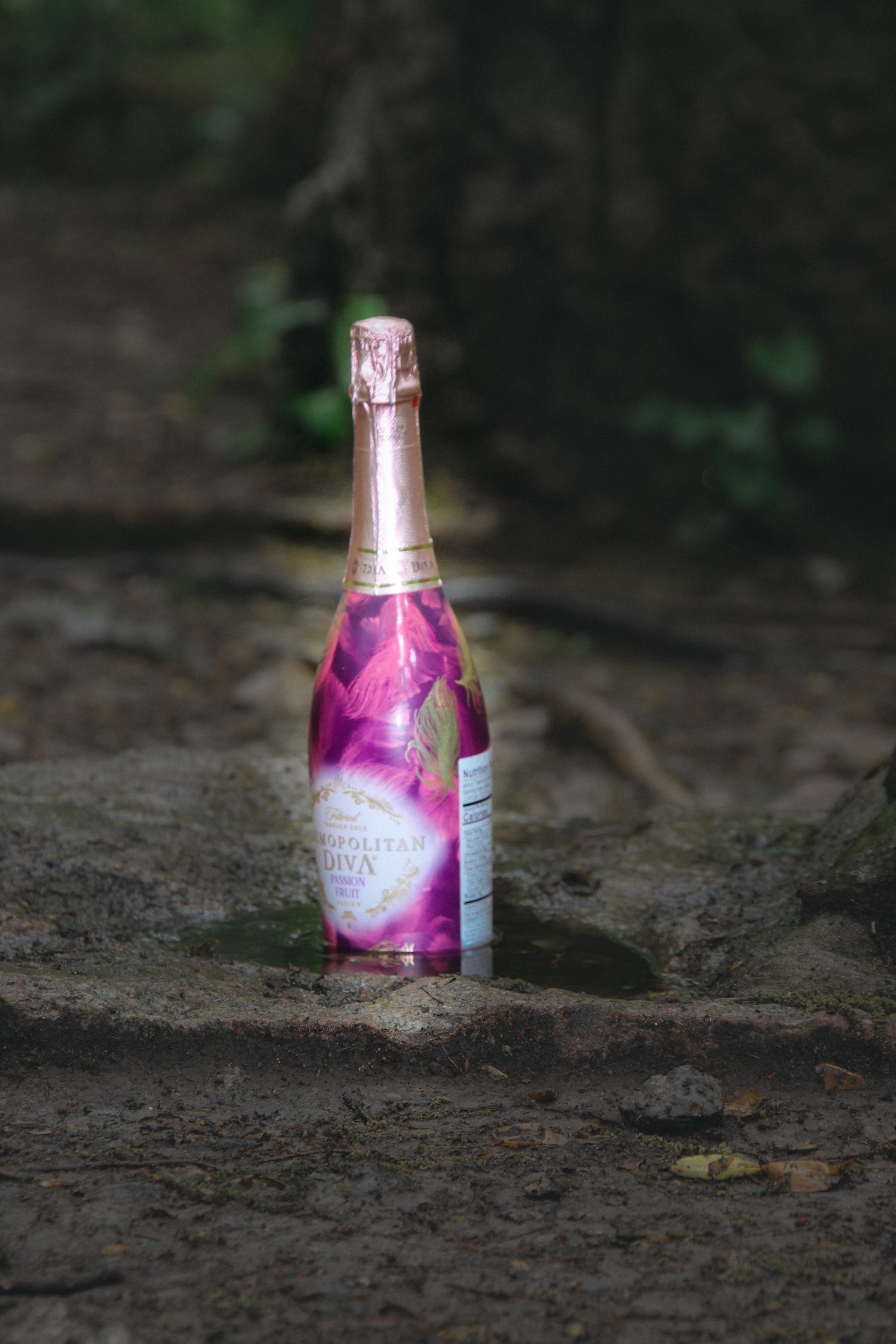 A pink beverage bottle sits on dark ground in a progression of four sequential shots showing different angles.