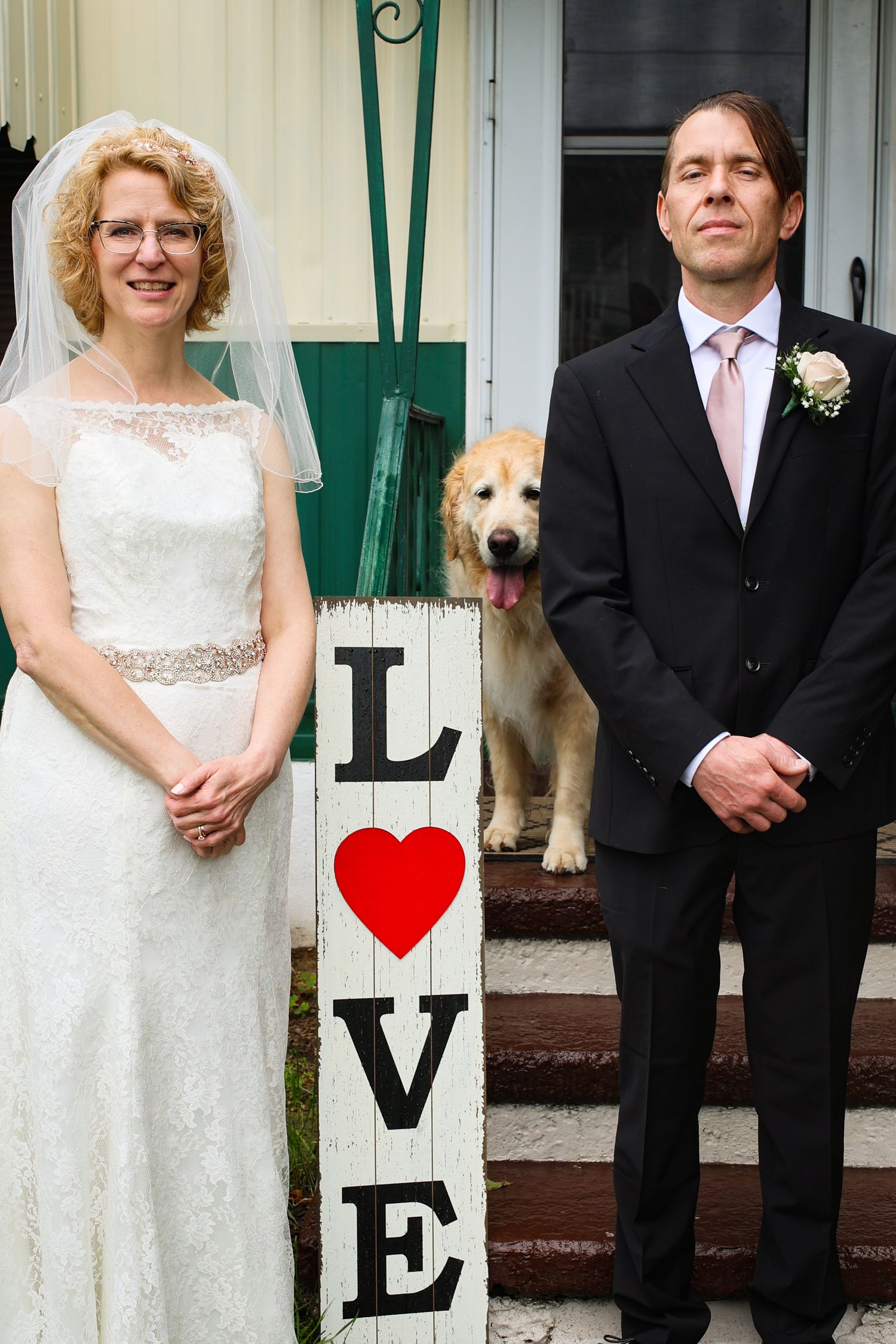 Wedding couple poses with their dog on steps with decorative LOVE letters and red hearts.