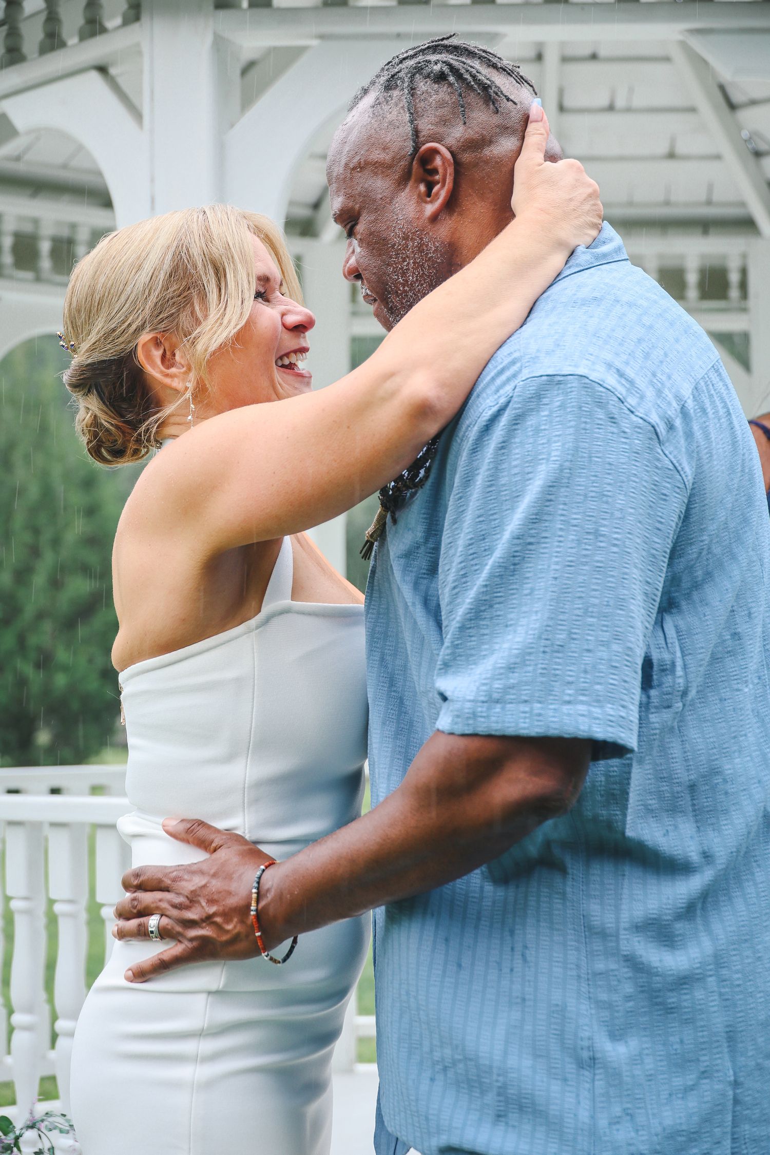 A couple in white and blue clothing dance together on an outdoor patio with white railings.