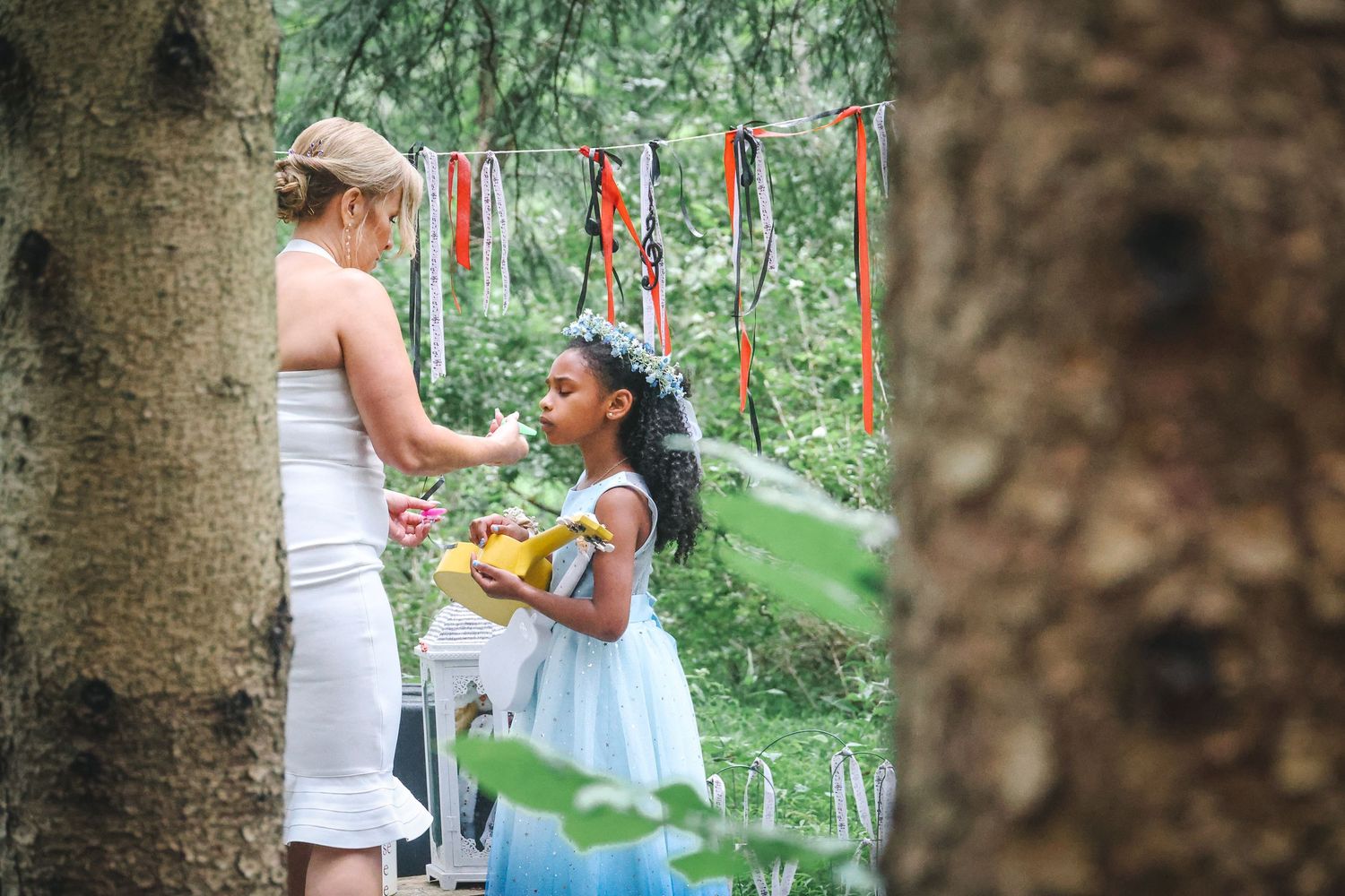 A couple in white clothing shares a romantic moment in a lush garden setting during what appears to be a wedding ceremony.