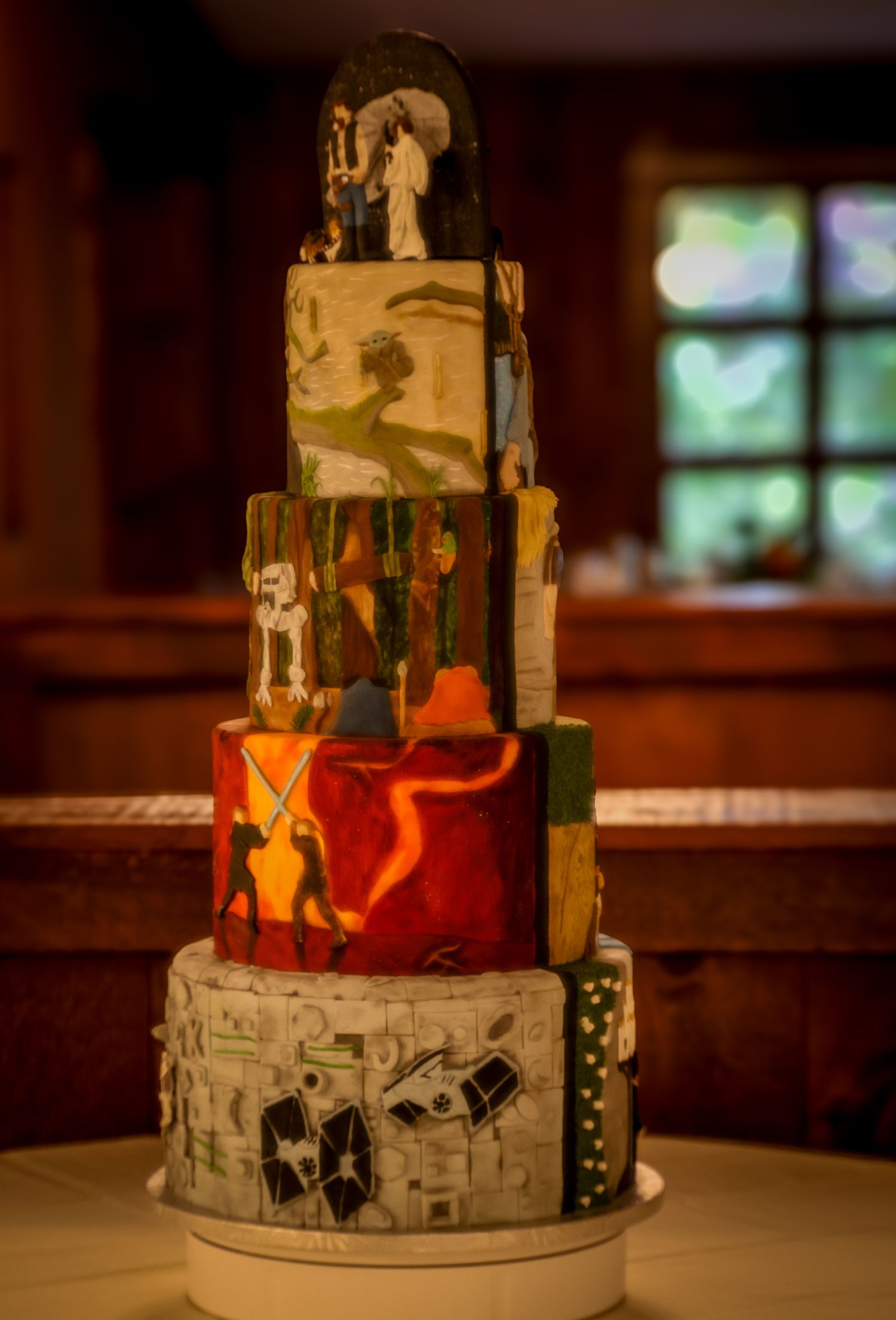 A multi-tiered wedding cake decorated with Star Wars themed designs and characters in orange and gray colors.