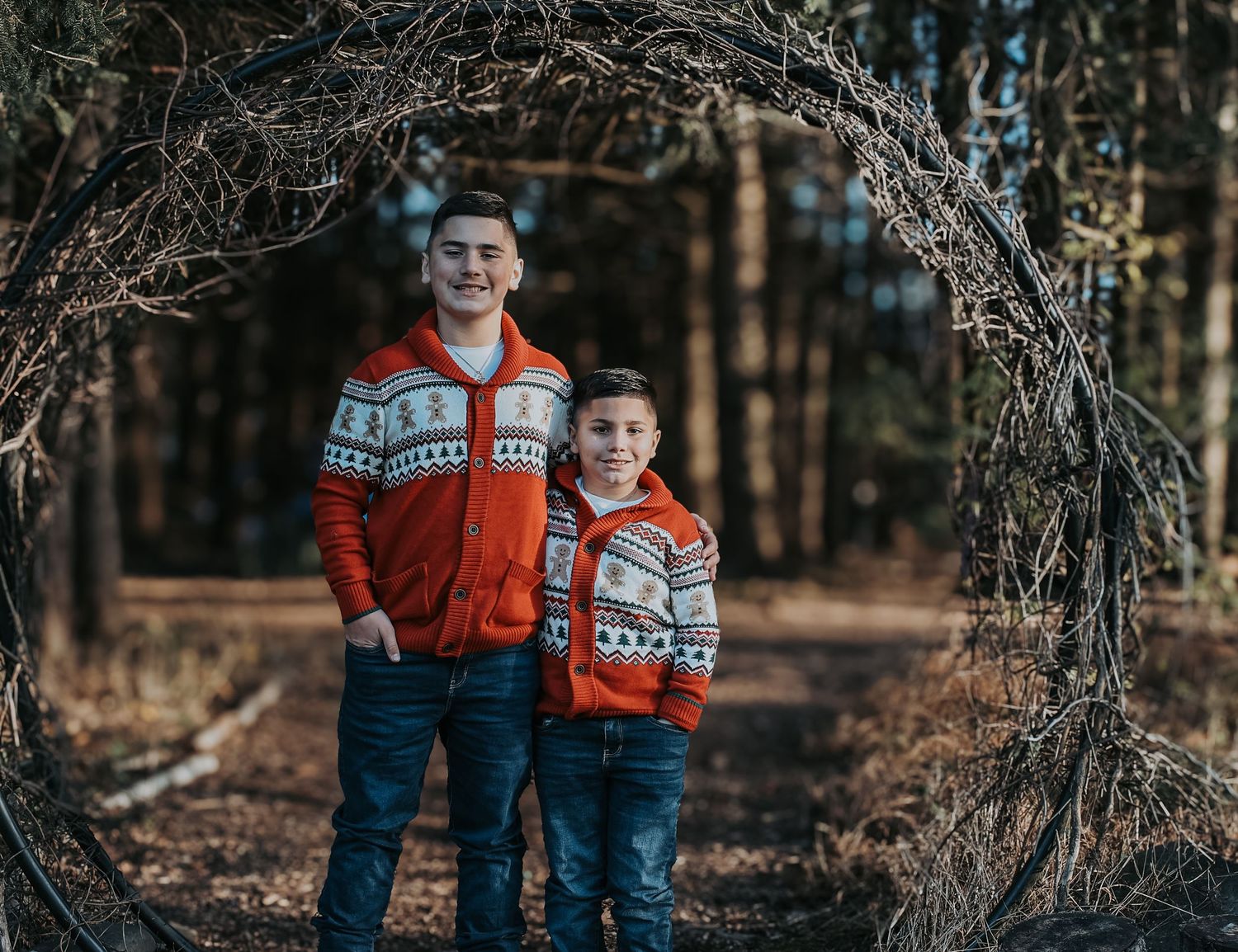 Family wearing coordinated winter sweaters poses together in a rustic autumn forest setting.