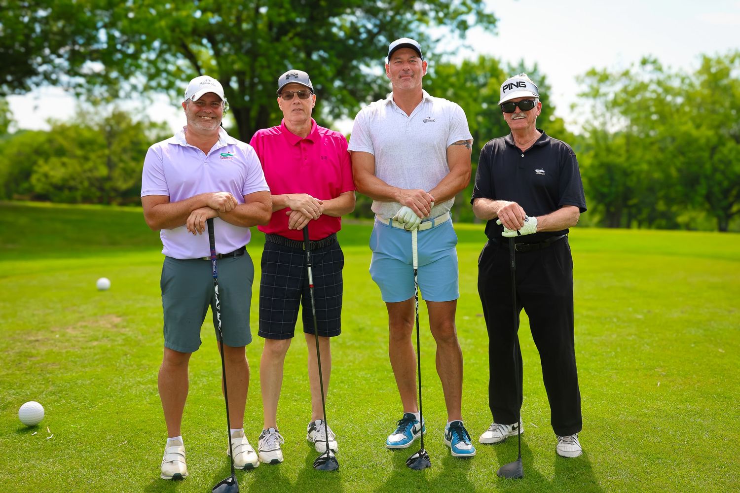 Golfers stand on a lush green course with their clubs during a sunny day at the golf club.