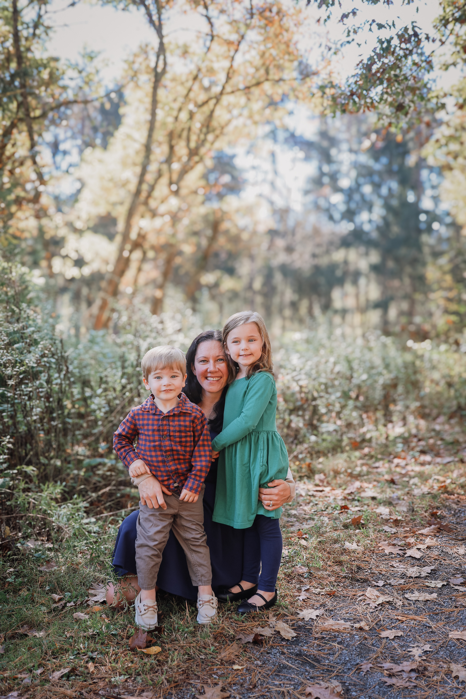 A family sits together outdoors in an autumn forest setting with fallen leaves and natural lighting.