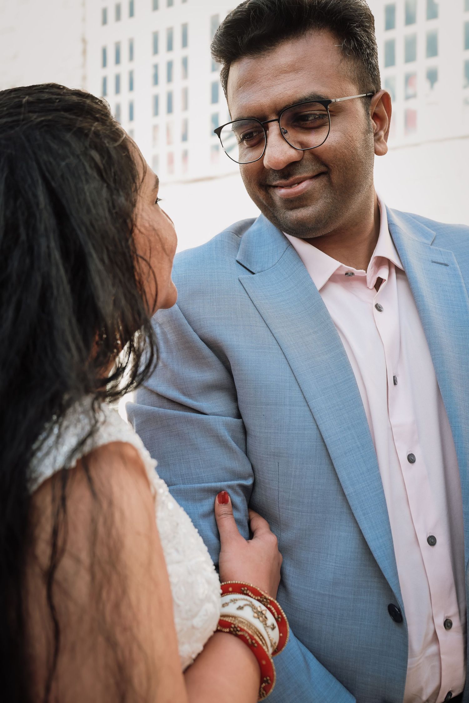 A couple in formal attire share an intimate moment against a white building backdrop.