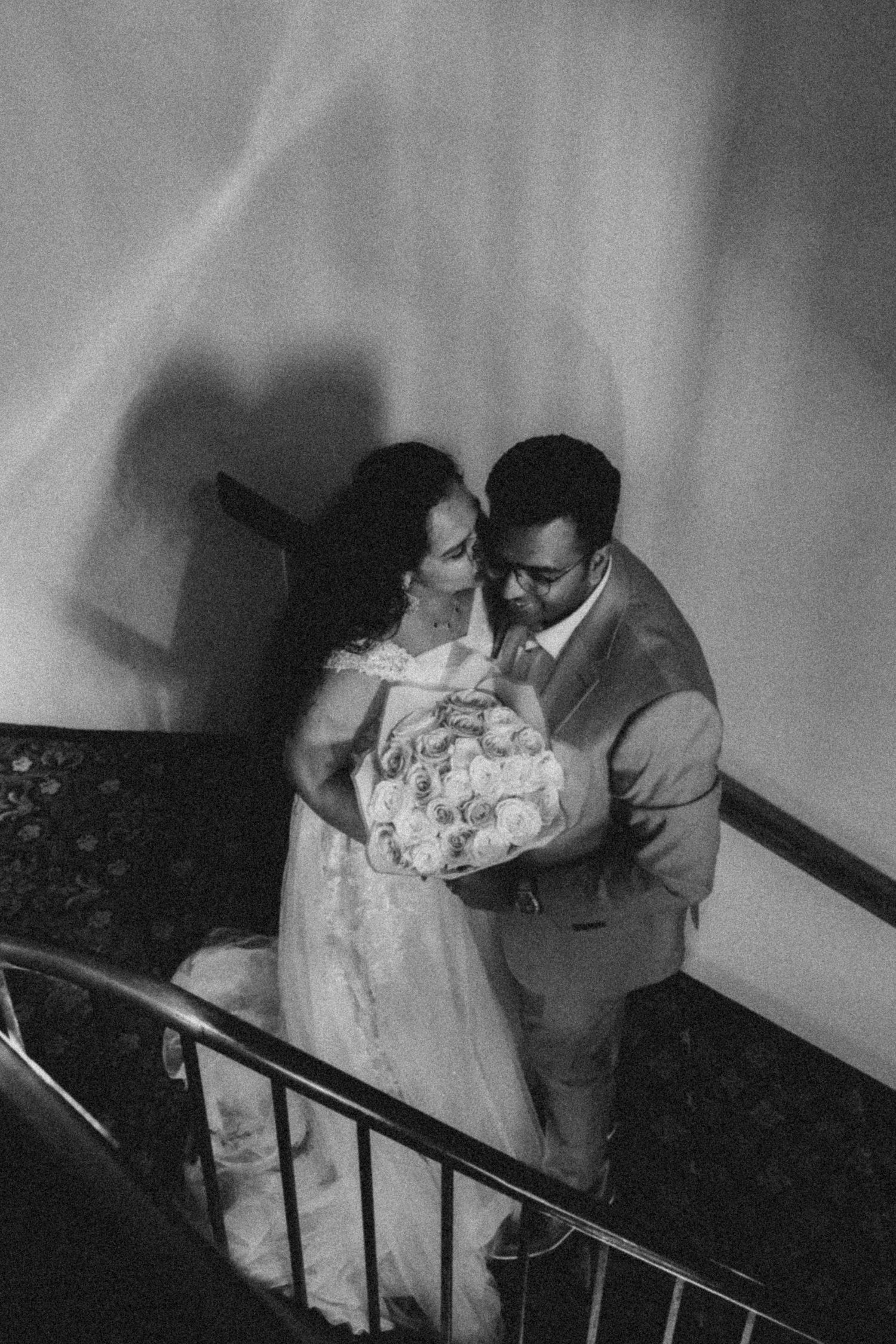 A couple in formal attire descends a dimly lit staircase in this vintage black and white photograph.